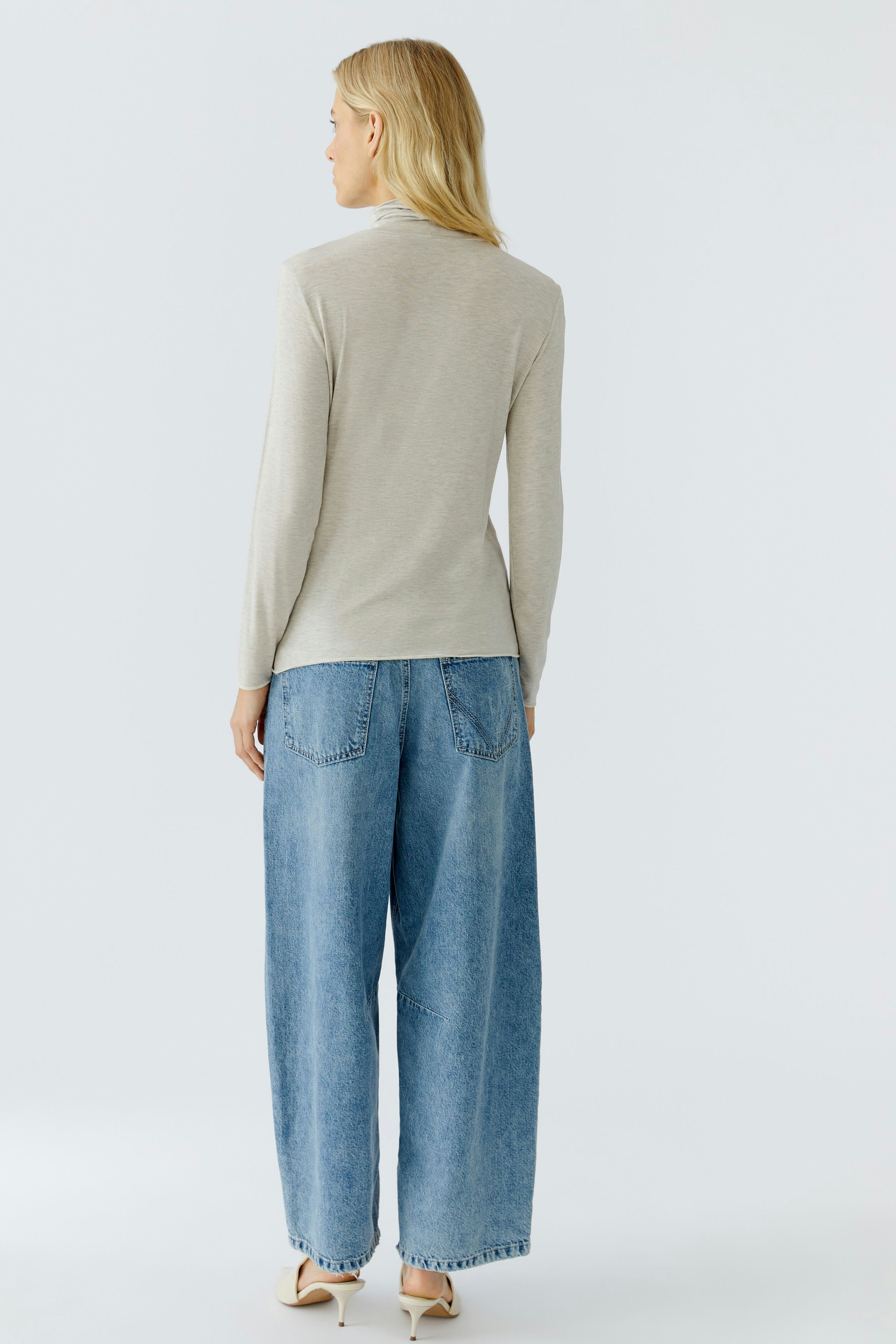 Casual long-sleeve shirt: Woman in a light gray pullover paired with wide-leg jeans, showcasing a relaxed style.