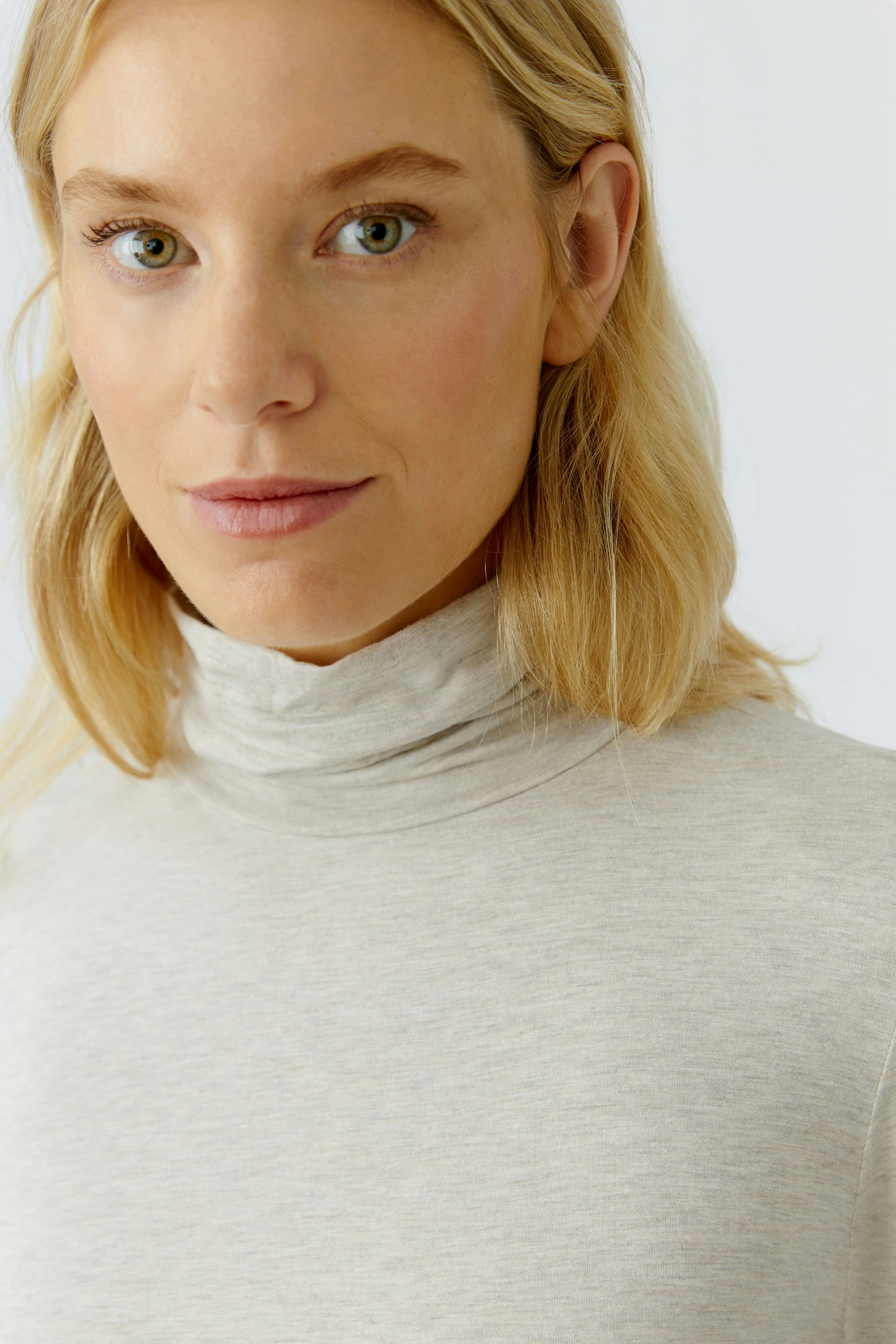 Casual women's long-sleeve shirt: A woman in a light gray turtleneck top with a relaxed fit.
