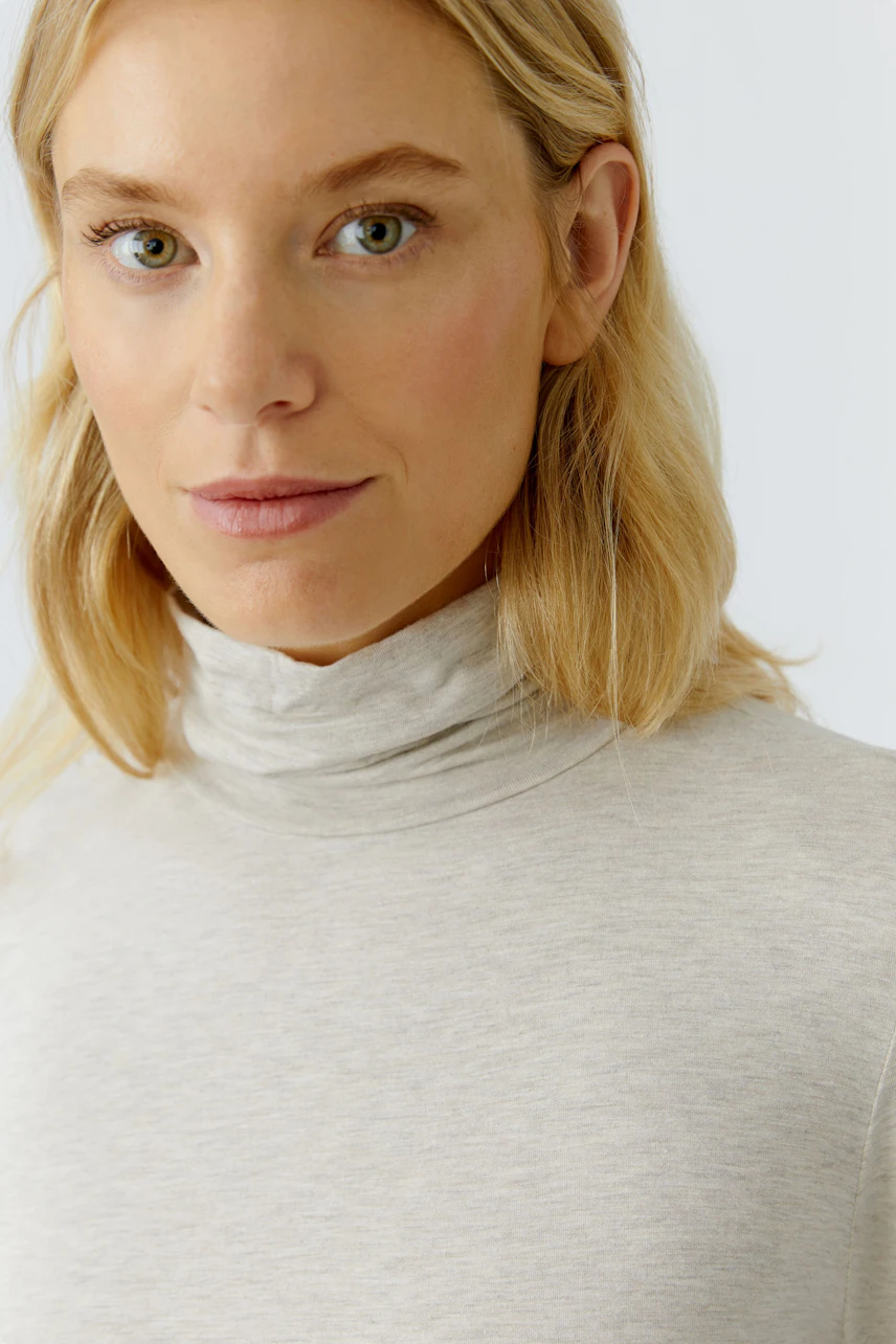 Casual women's long-sleeve shirt: A woman in a light gray turtleneck top with a relaxed fit.