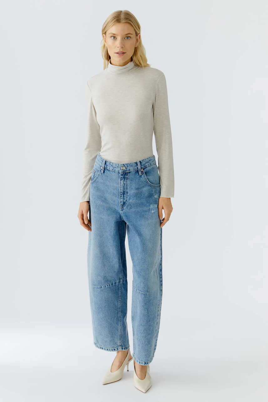 Casual women's long-sleeve shirt: Woman in a light beige top paired with relaxed-fit jeans.