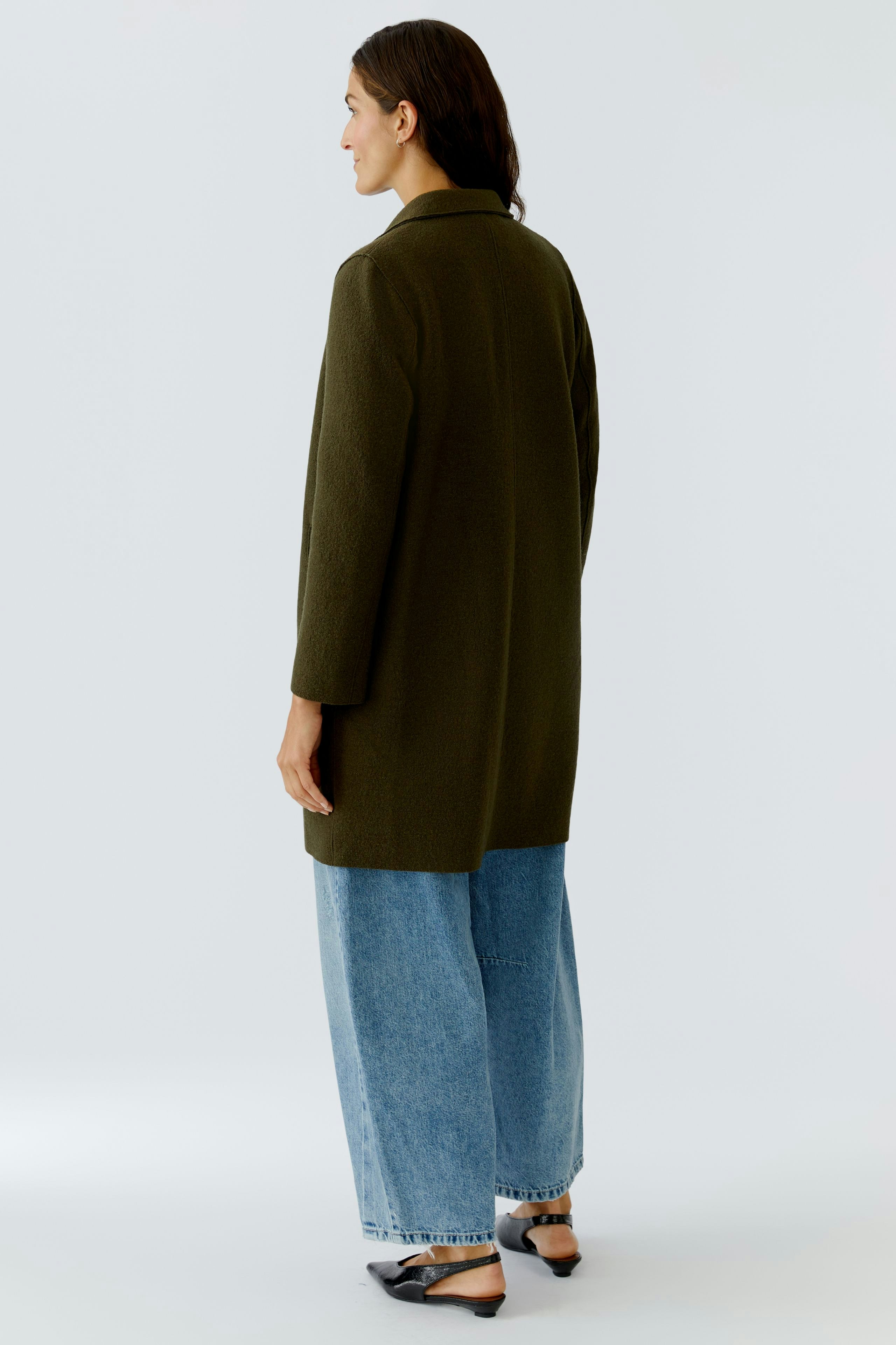 Damen Wollmantel: Frau in grünem Wollmantel mit lässigen Jeans und Schuhen, von hinten sichtbar.