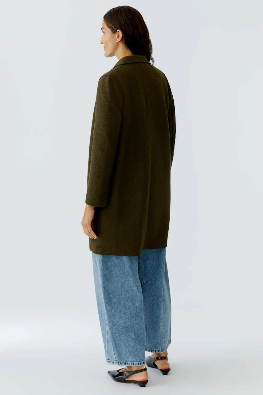 Damen Wollmantel: Frau in grünem Wollmantel mit lässigen Jeans und Schuhen, von hinten sichtbar.