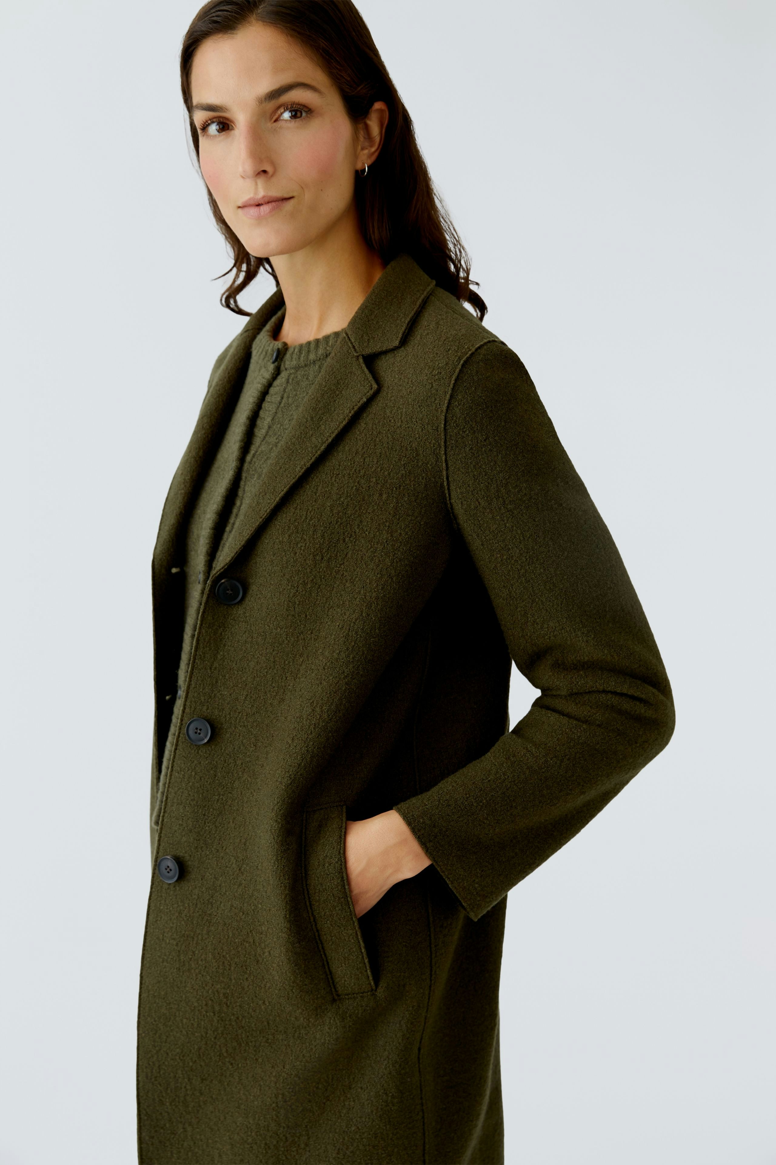 Damen Wollmantel: Frau in olivgrünem Mantel mit Knöpfen und Taschen, lässig und modern.