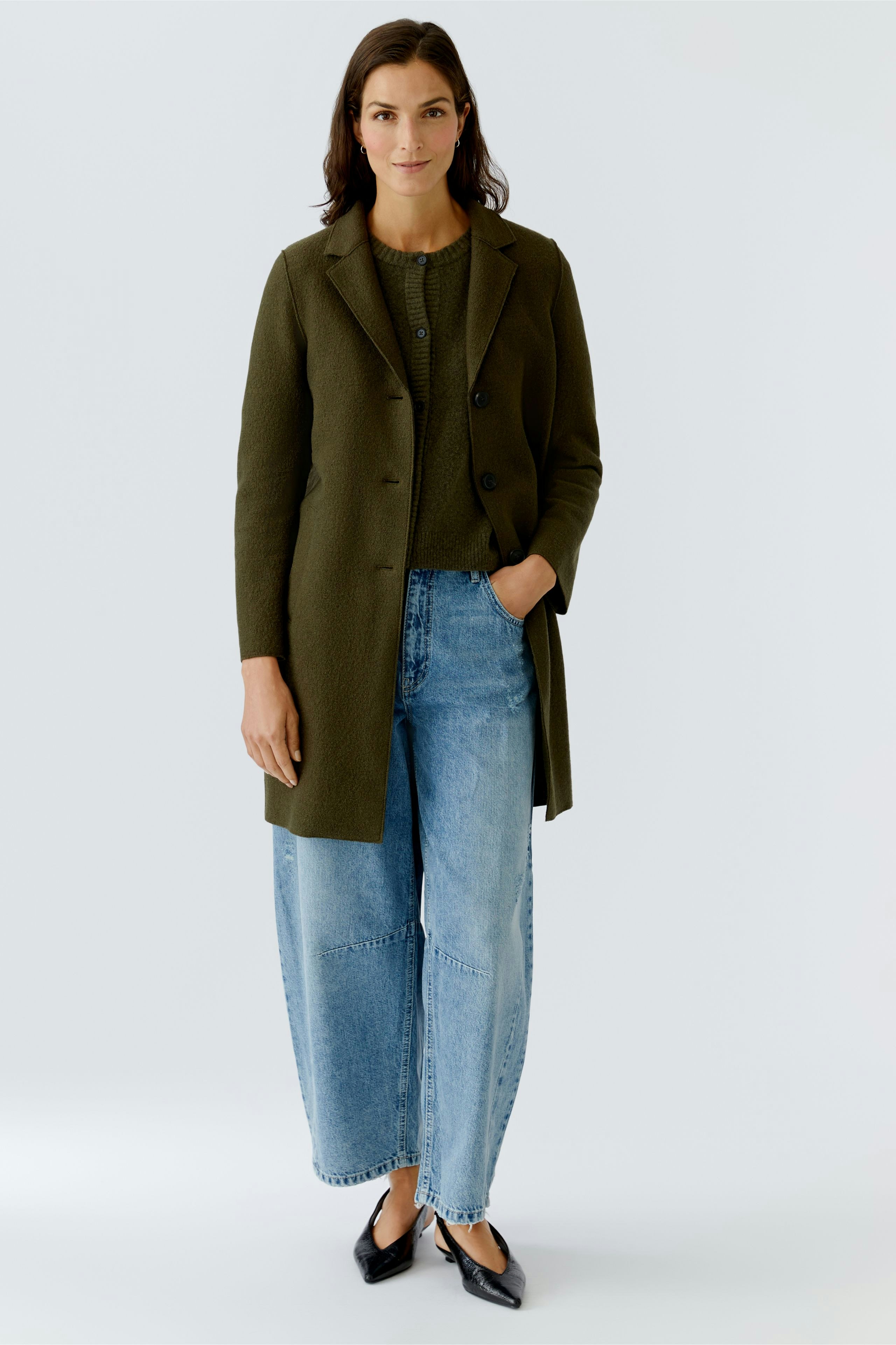 Damen Wollmantel: Frau in olivgrünem Mantel über lässigem Outfit mit Jeans und Bluse.