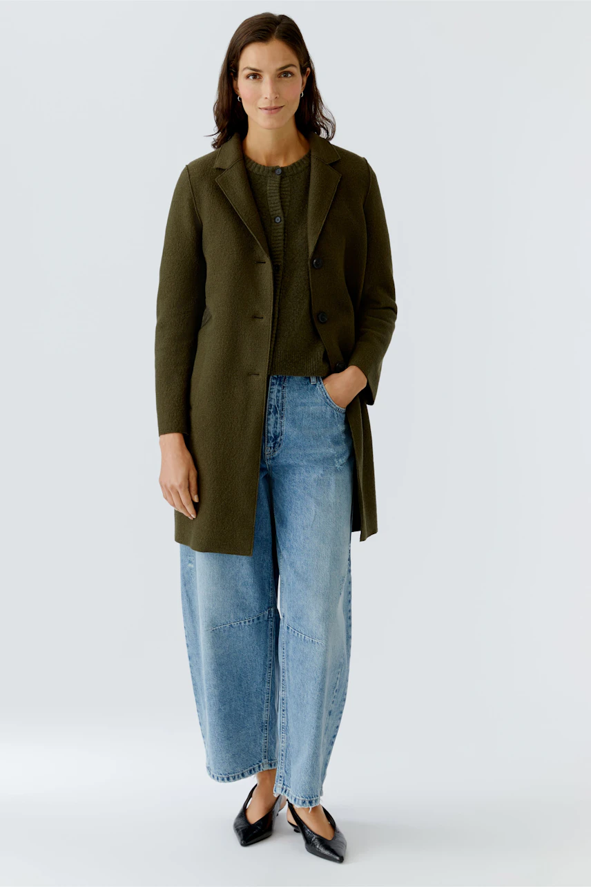 Damen Wollmantel: Frau in olivgrünem Mantel über lässigem Outfit mit Jeans und Bluse.
