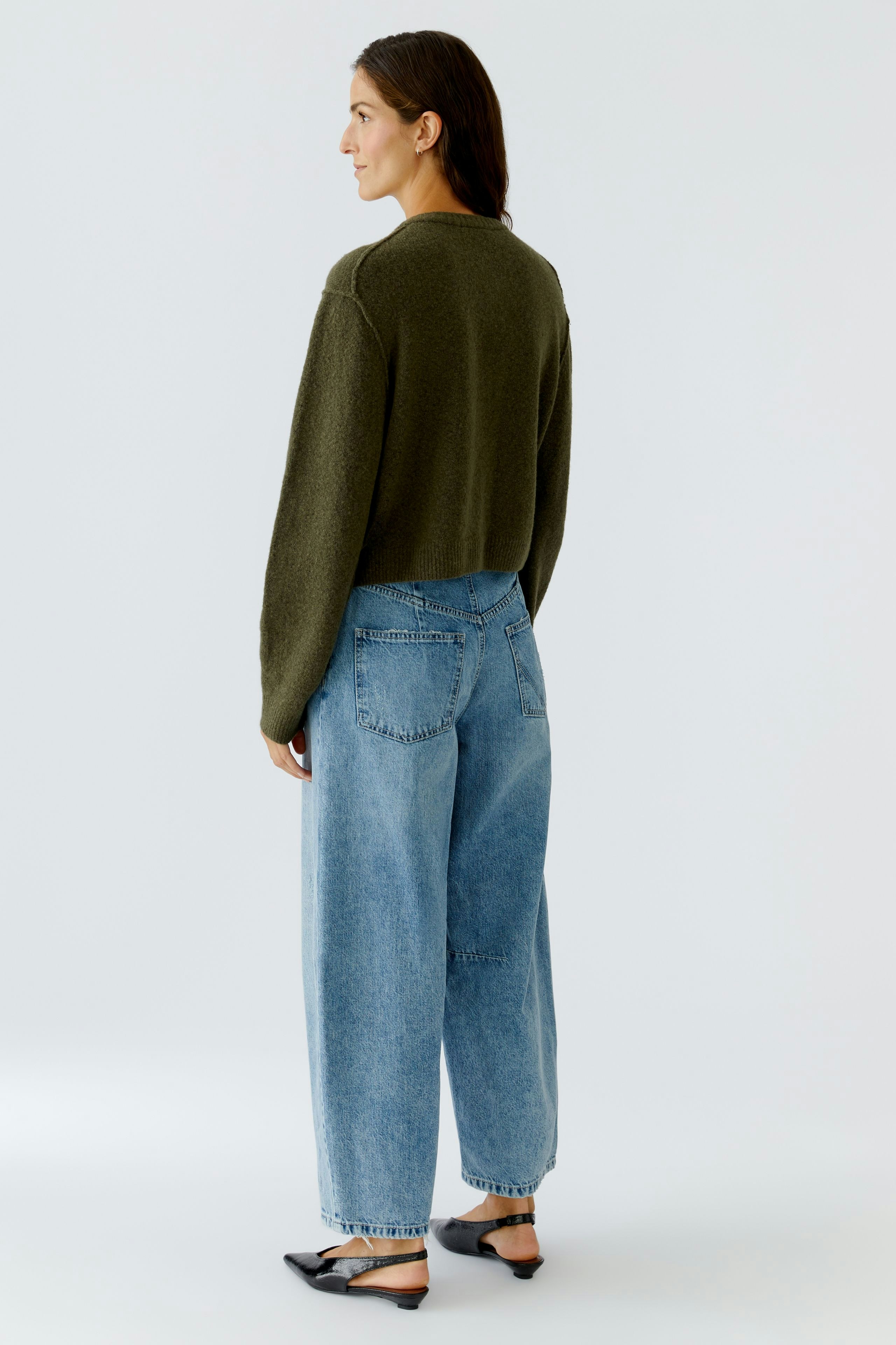 Damen-Strickjacke: Frau in olivgrüner Strickjacke mit lässigen Jeans und Schuhen, von hinten sichtbar.