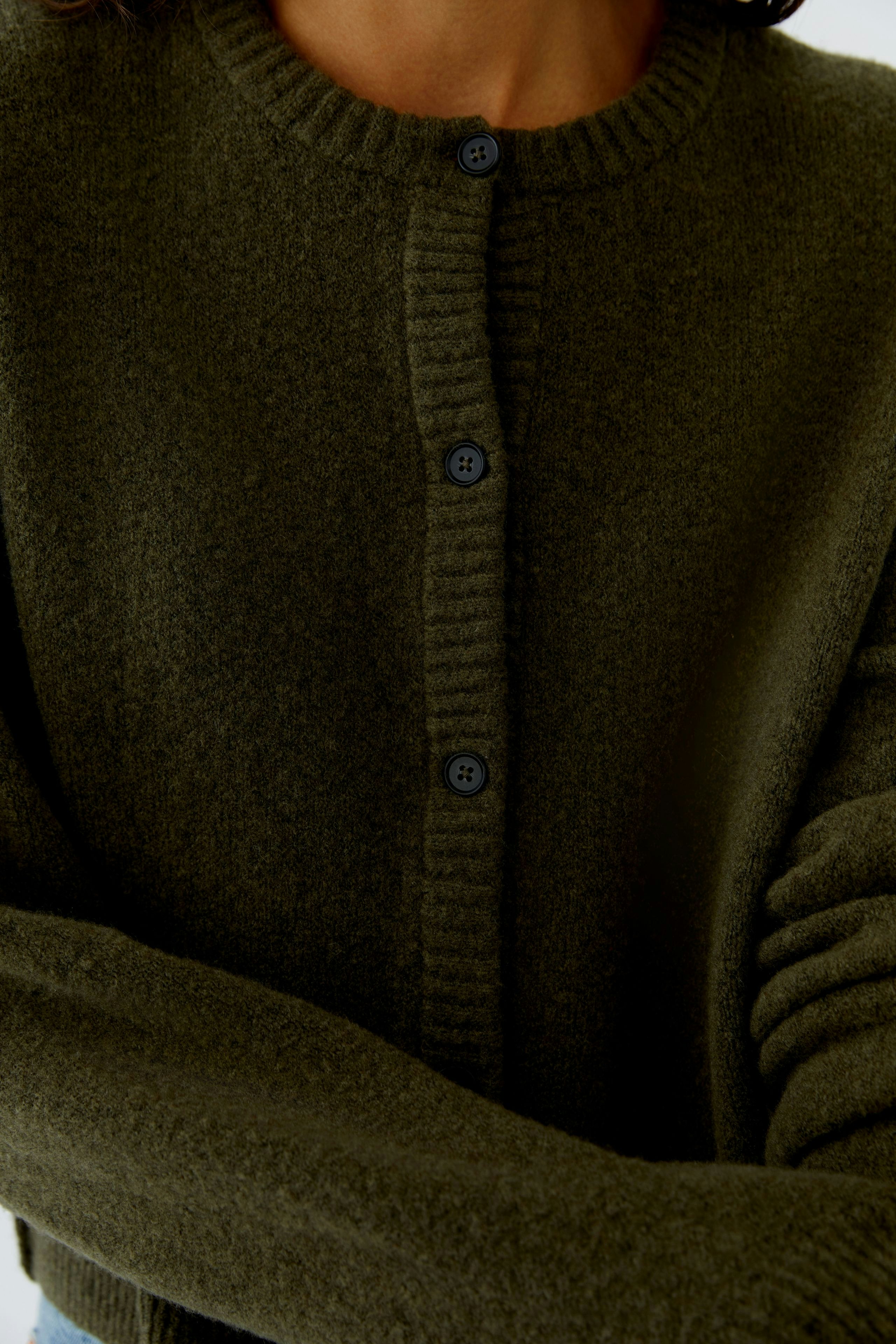 Damen-Strickjacke: Frau in olivgrüner Strickjacke mit Knöpfen und lässigem Schnitt.