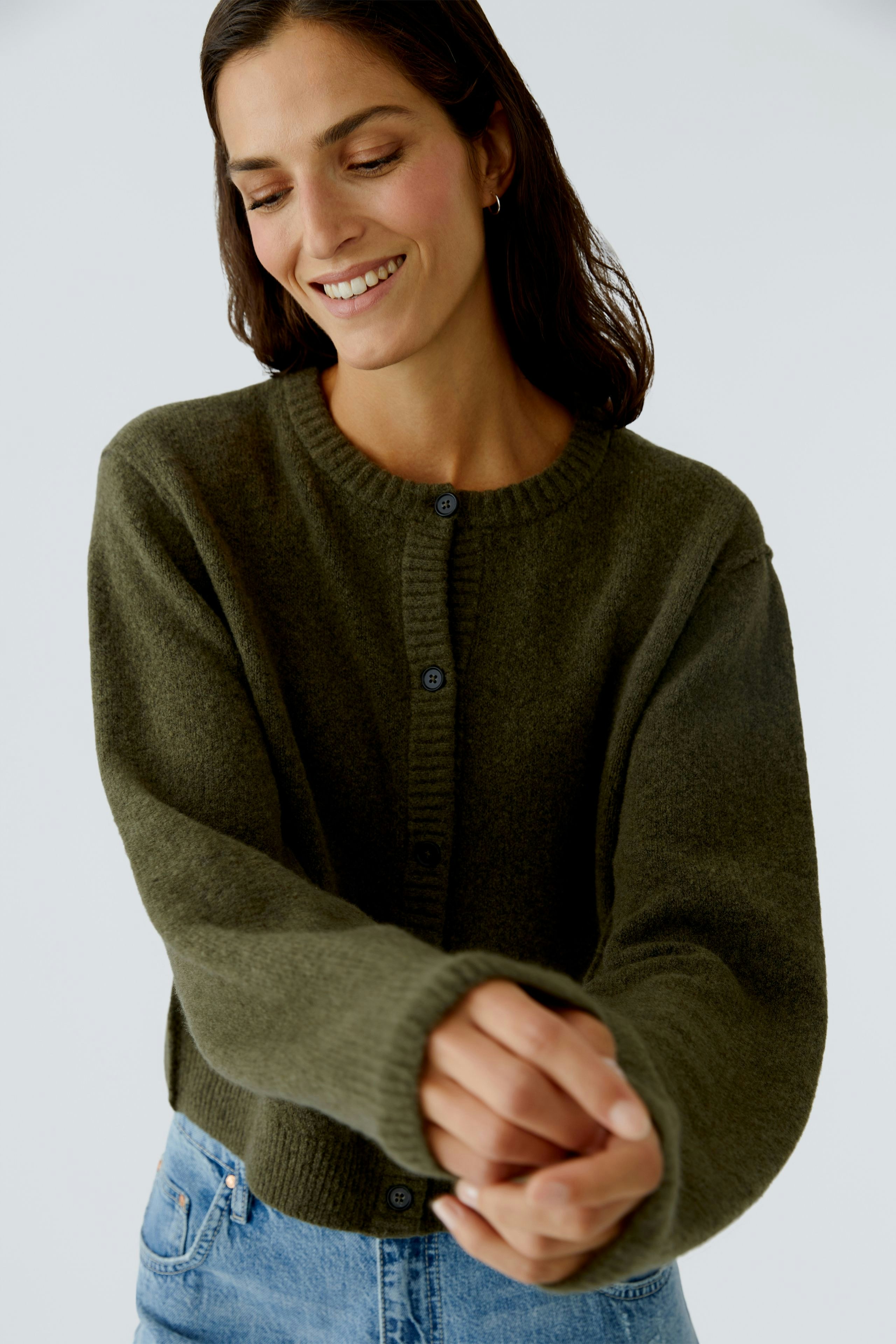 Damen-Strickjacke: Frau in olivgrüner Strickjacke mit Knöpfen und lässigem Look lächelt freundlich.