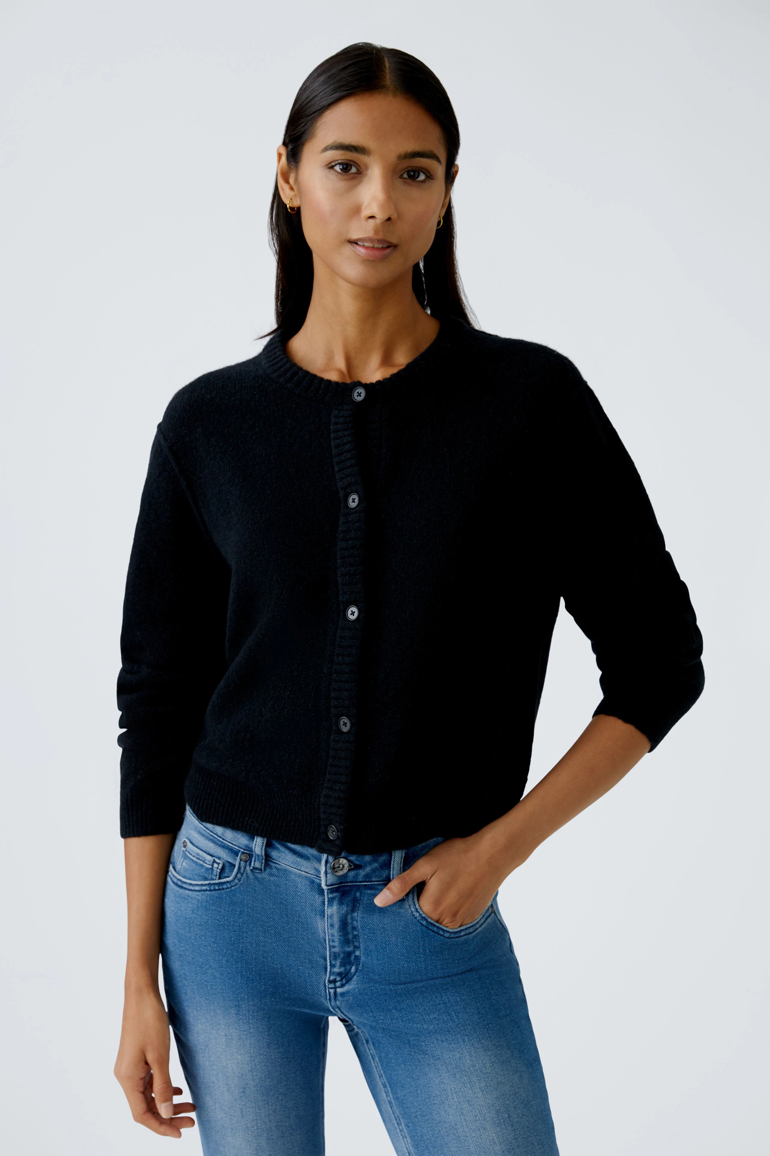 Schwarze Strickjacke: Junge Frau trägt eine bequeme Strickjacke mit Knöpfen und lässigen Jeans.