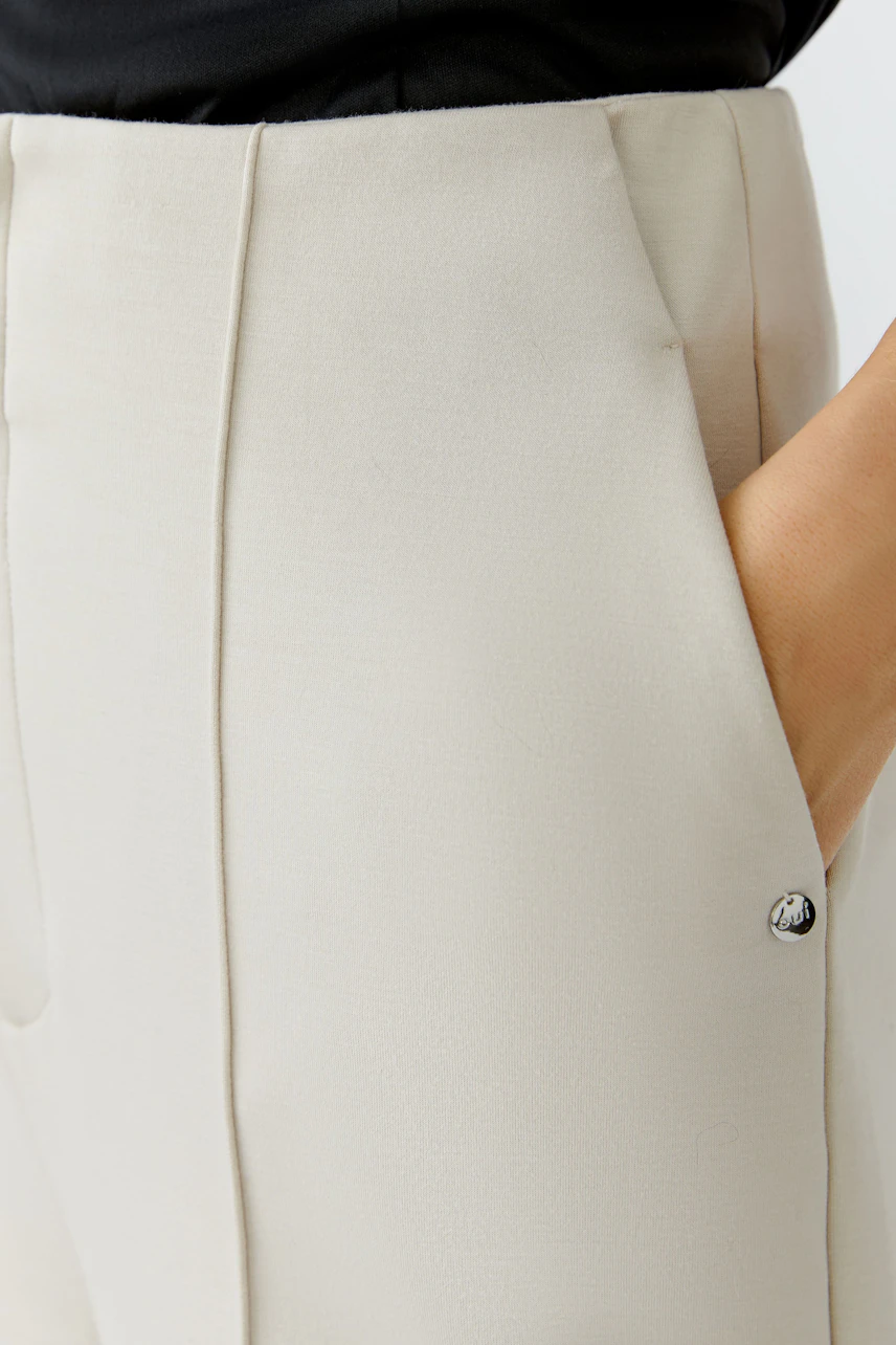 Bequeme Damen-Hose in hellem Beige mit seitlichen Taschen und dezentem Logo-Detail.