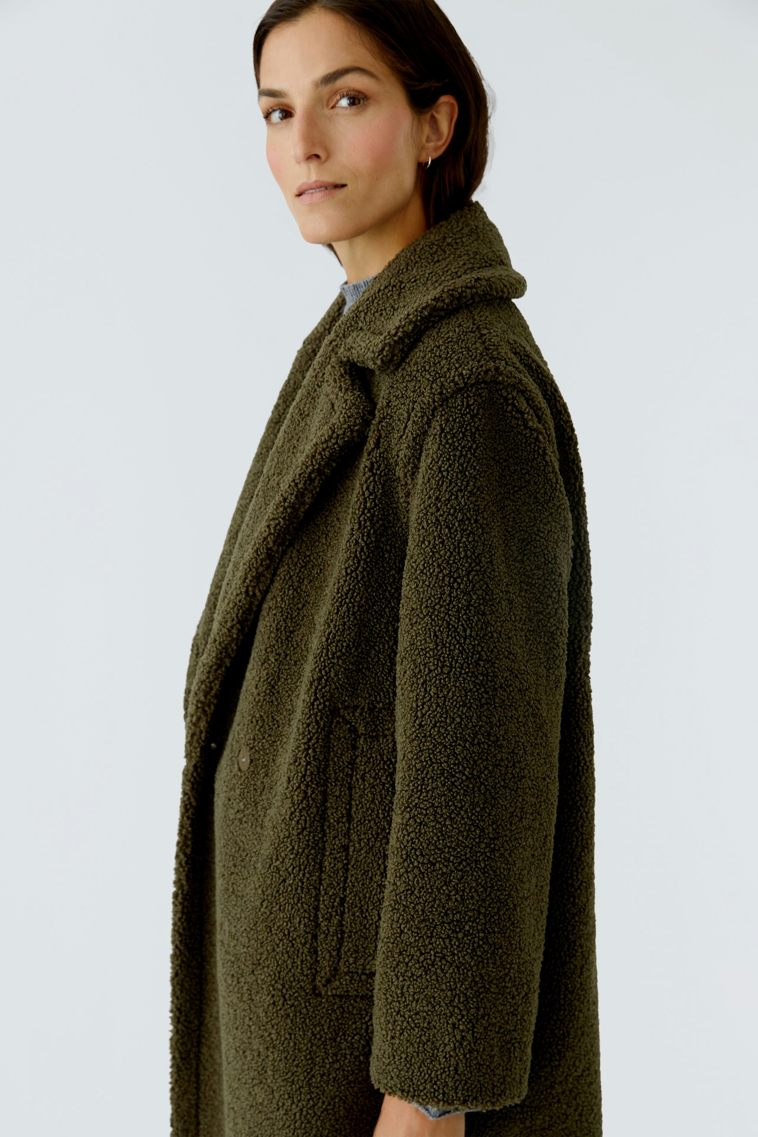 Cozy winter coat: Woman in a soft, olive green coat with a relaxed fit and large collar.