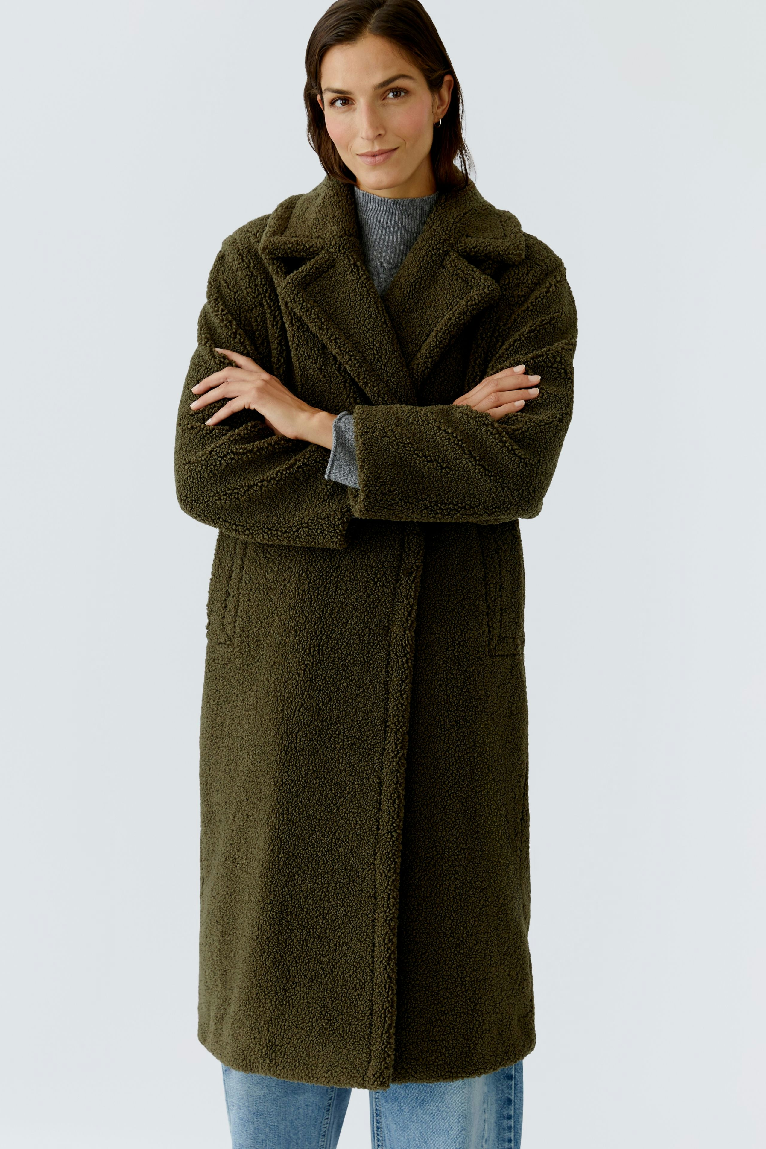 Cozy women's winter coat: A woman in a soft, olive green coat with a relaxed fit, arms crossed.