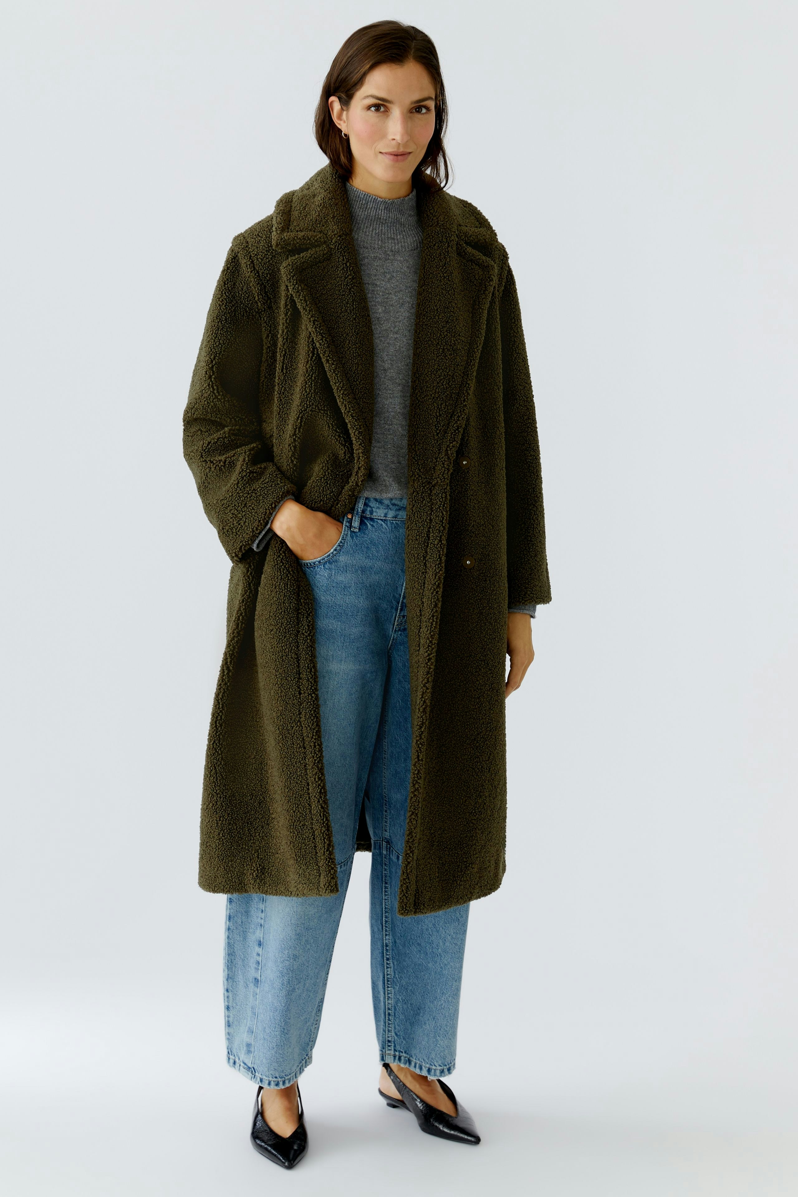 Cozy winter coat: Woman in an olive green coat over a gray pullover and relaxed jeans.