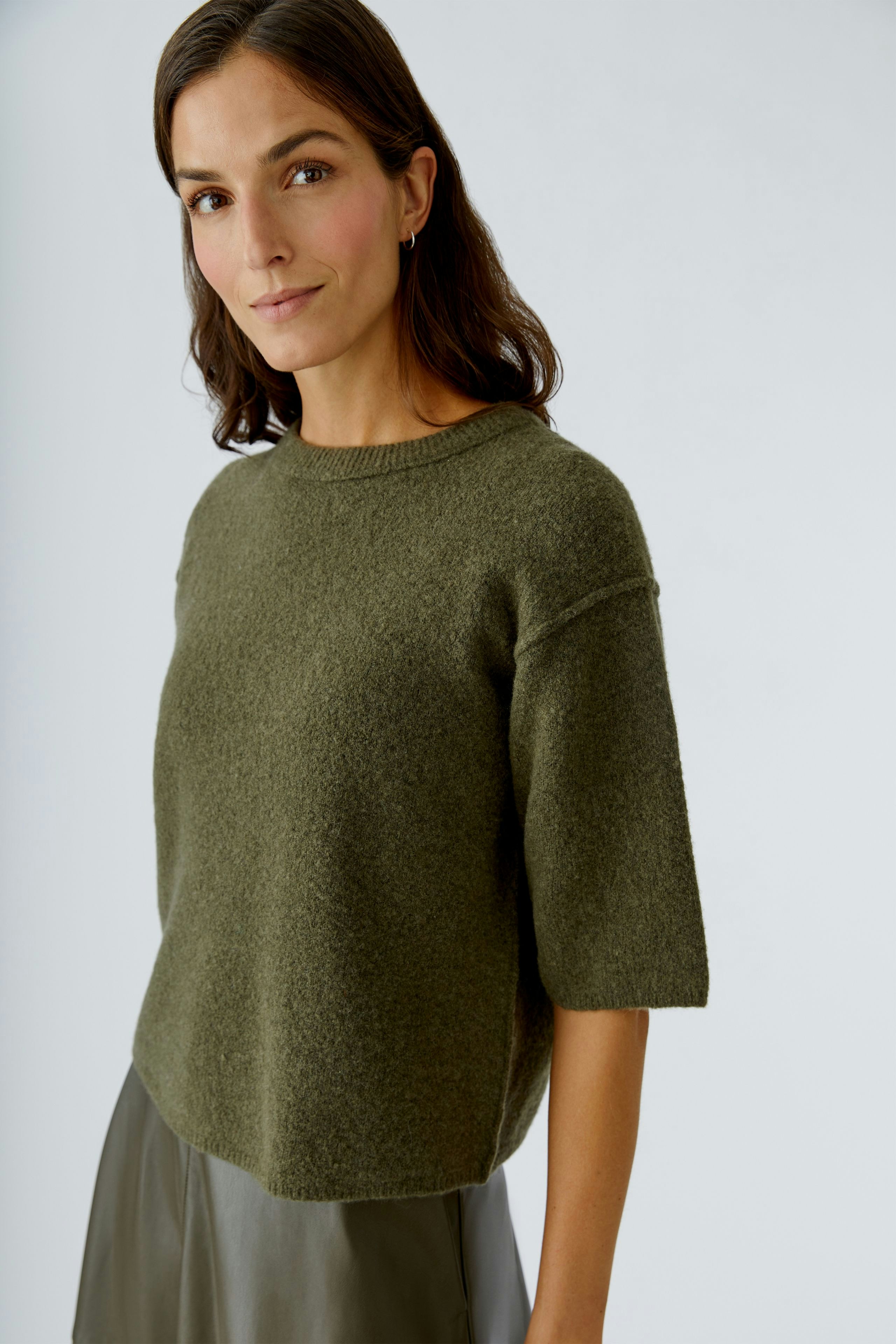 Casual women's pullover: Young woman in a short-sleeve, olive green pullover, smiling confidently.
