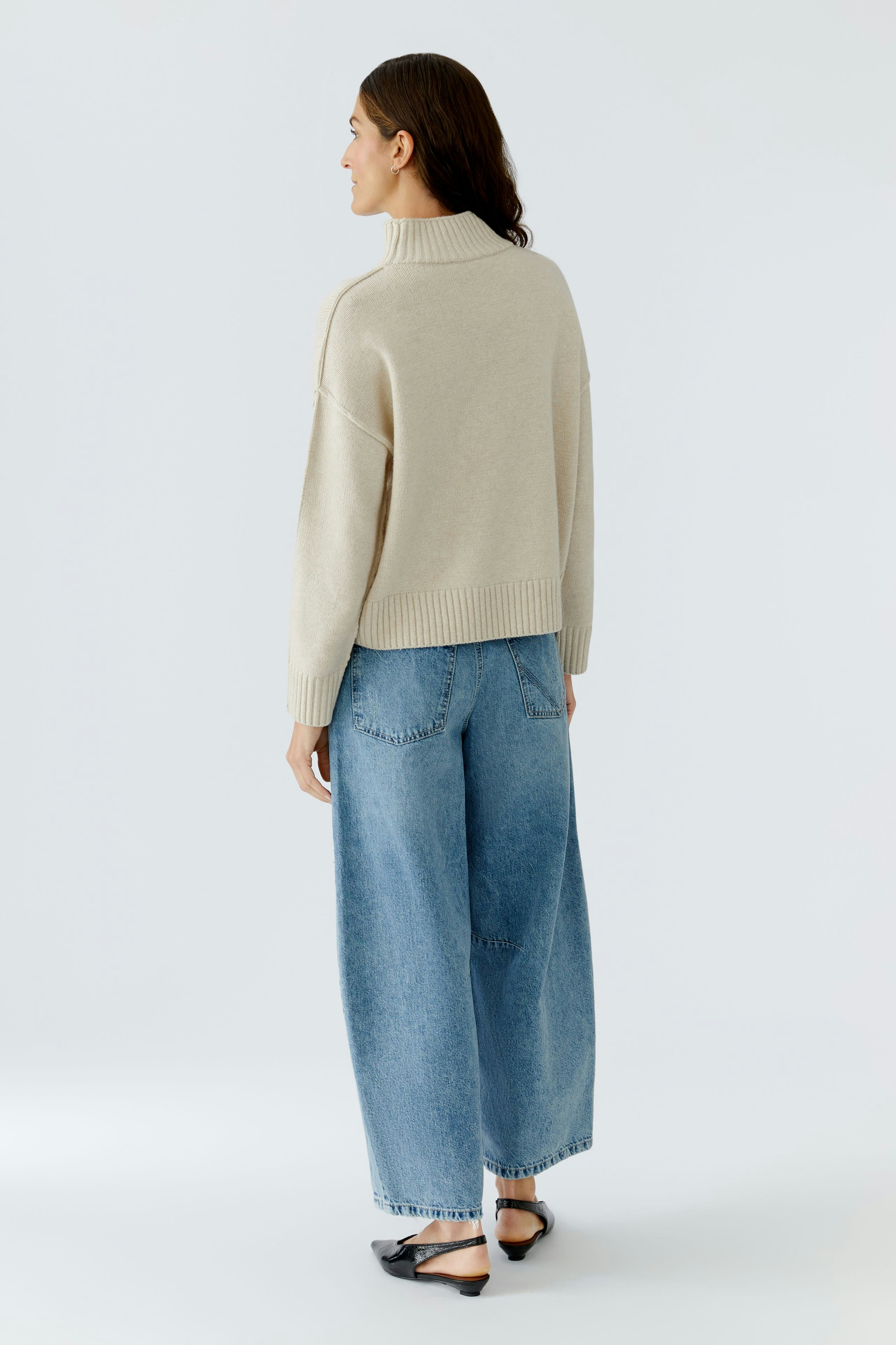Casual women's pullover: A woman in a beige pullover with a relaxed fit and wide jeans, seen from the back.