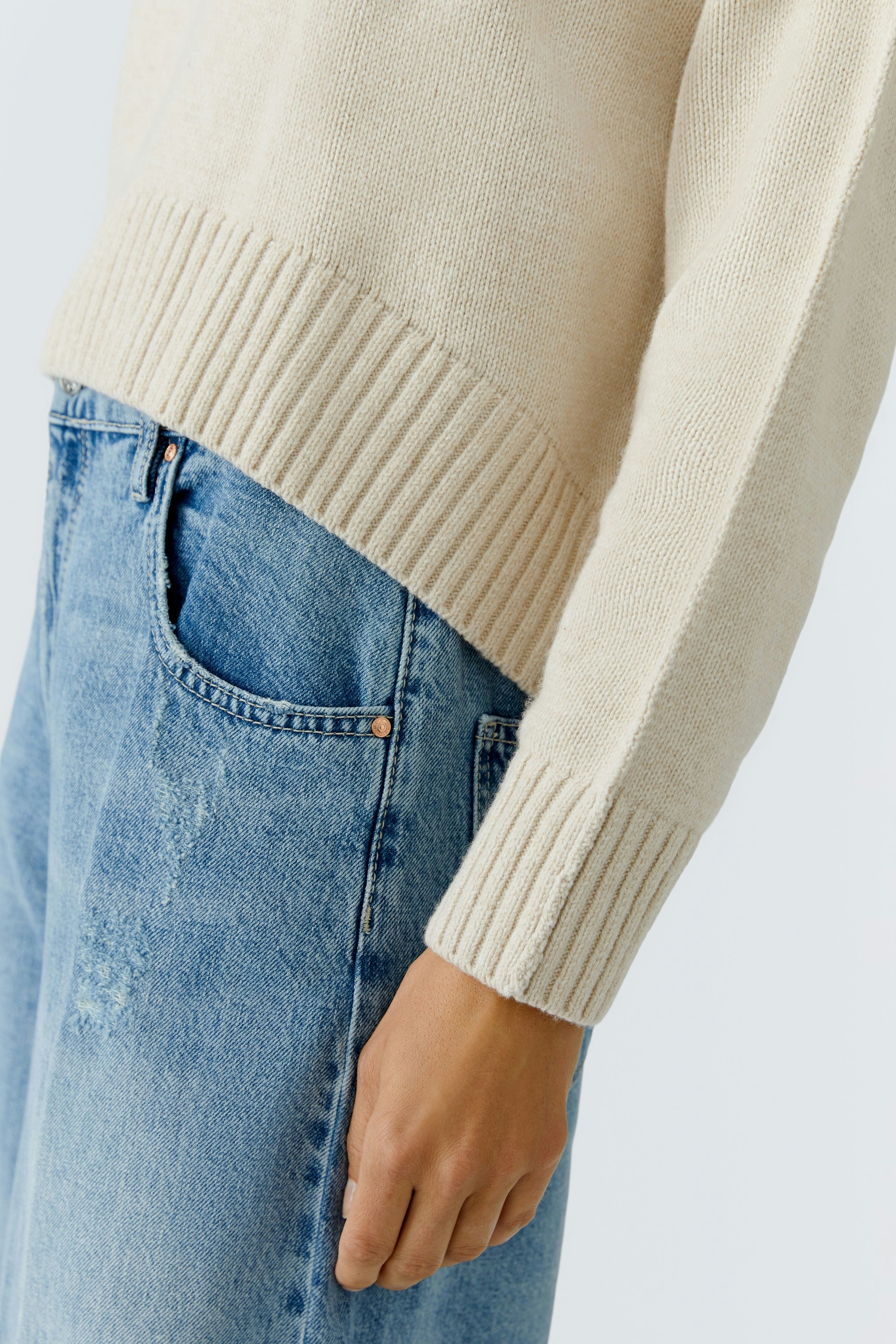 Casual women's pullover: Close-up of a light beige pullover with ribbed hem, paired with blue jeans.