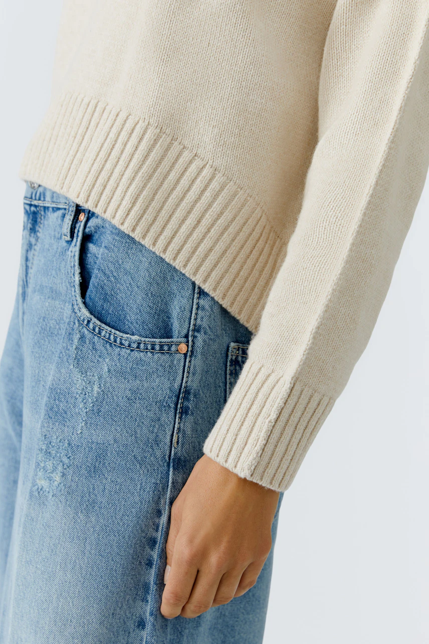 Casual women's pullover: Close-up of a light beige pullover with ribbed hem, paired with blue jeans.