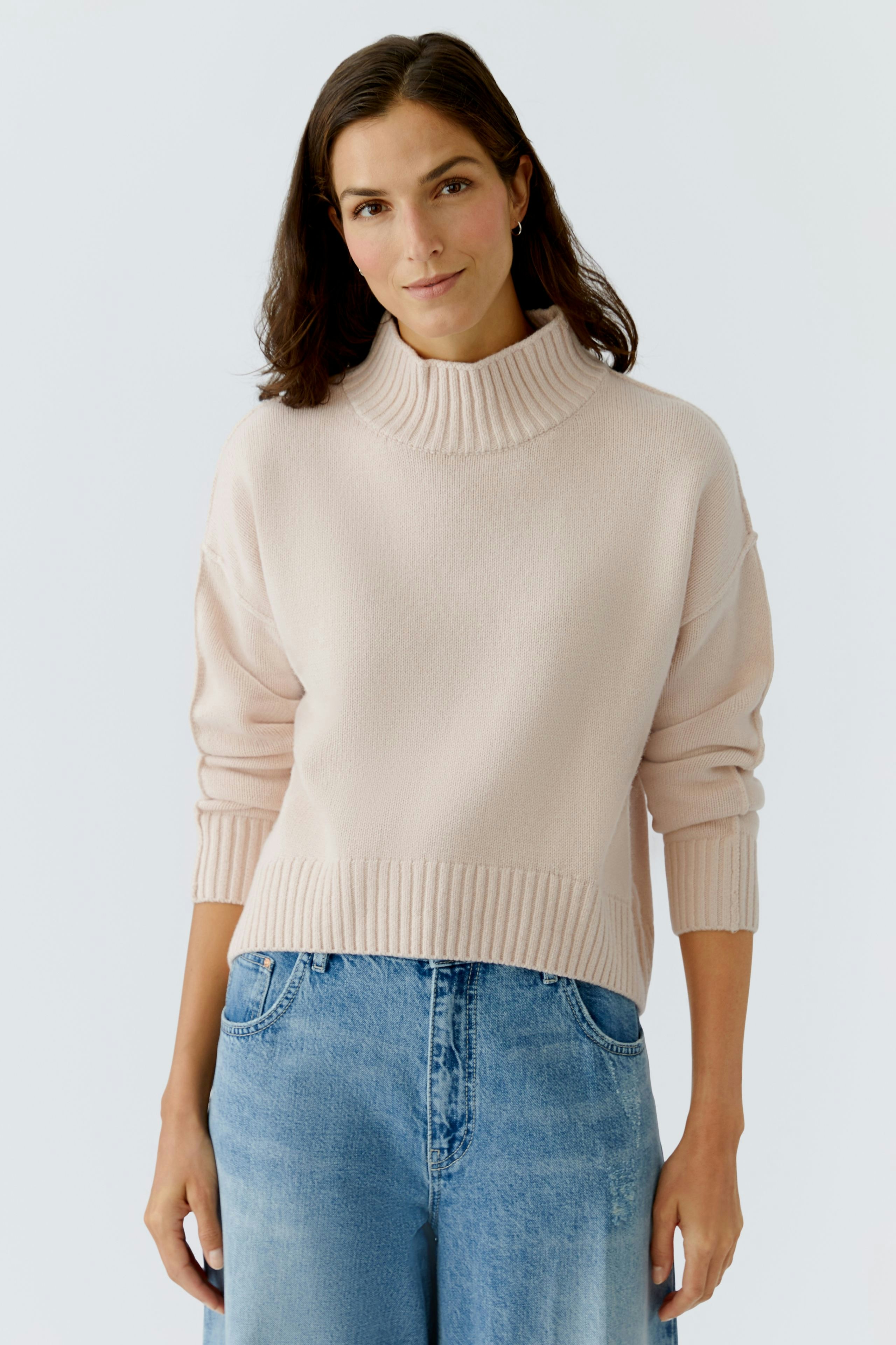 Casual women's pullover: A woman in a light pink pullover with a high neck and relaxed fit.