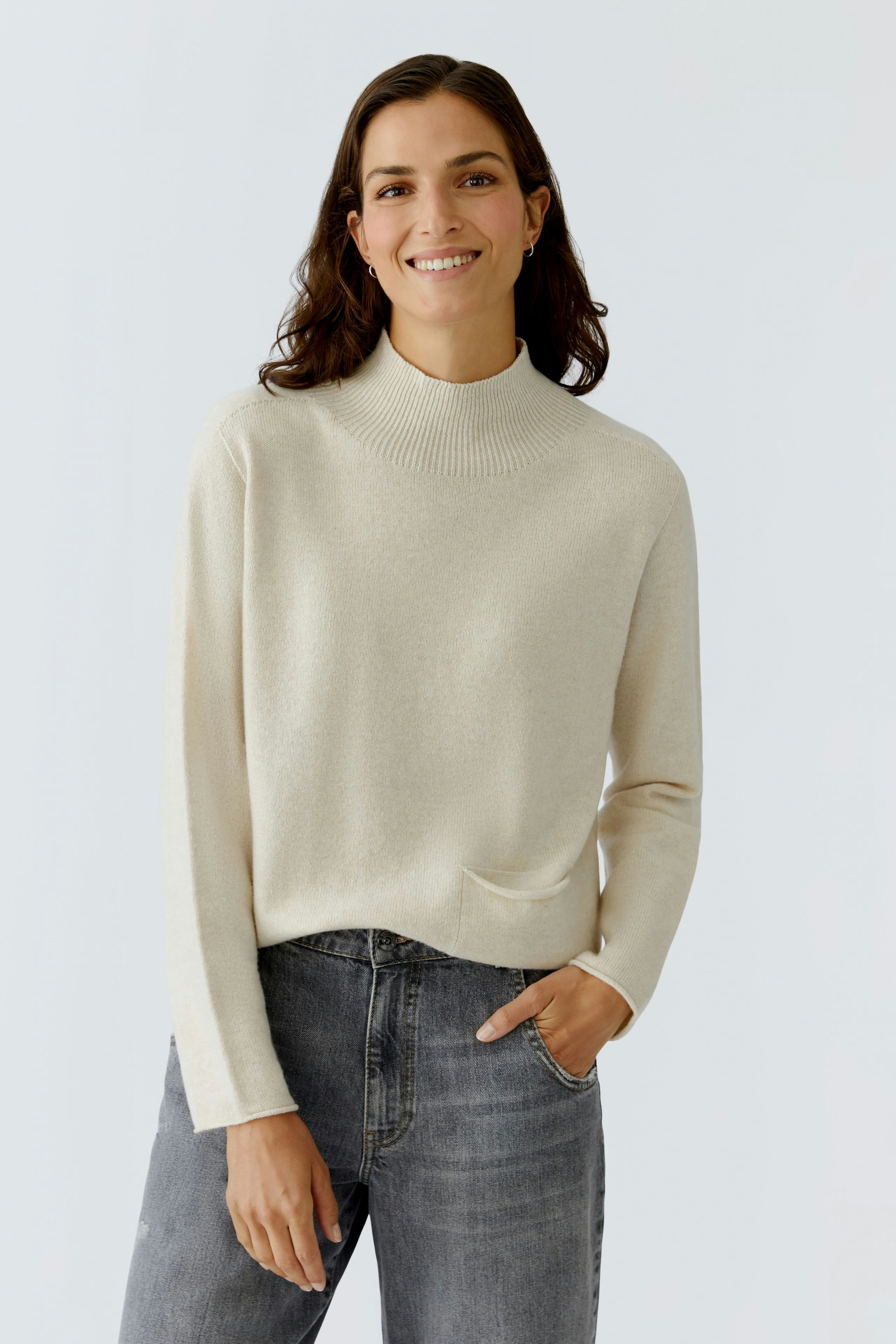 Modern women's pullover: Smiling woman in a cream pullover with a pocket, paired with jeans.