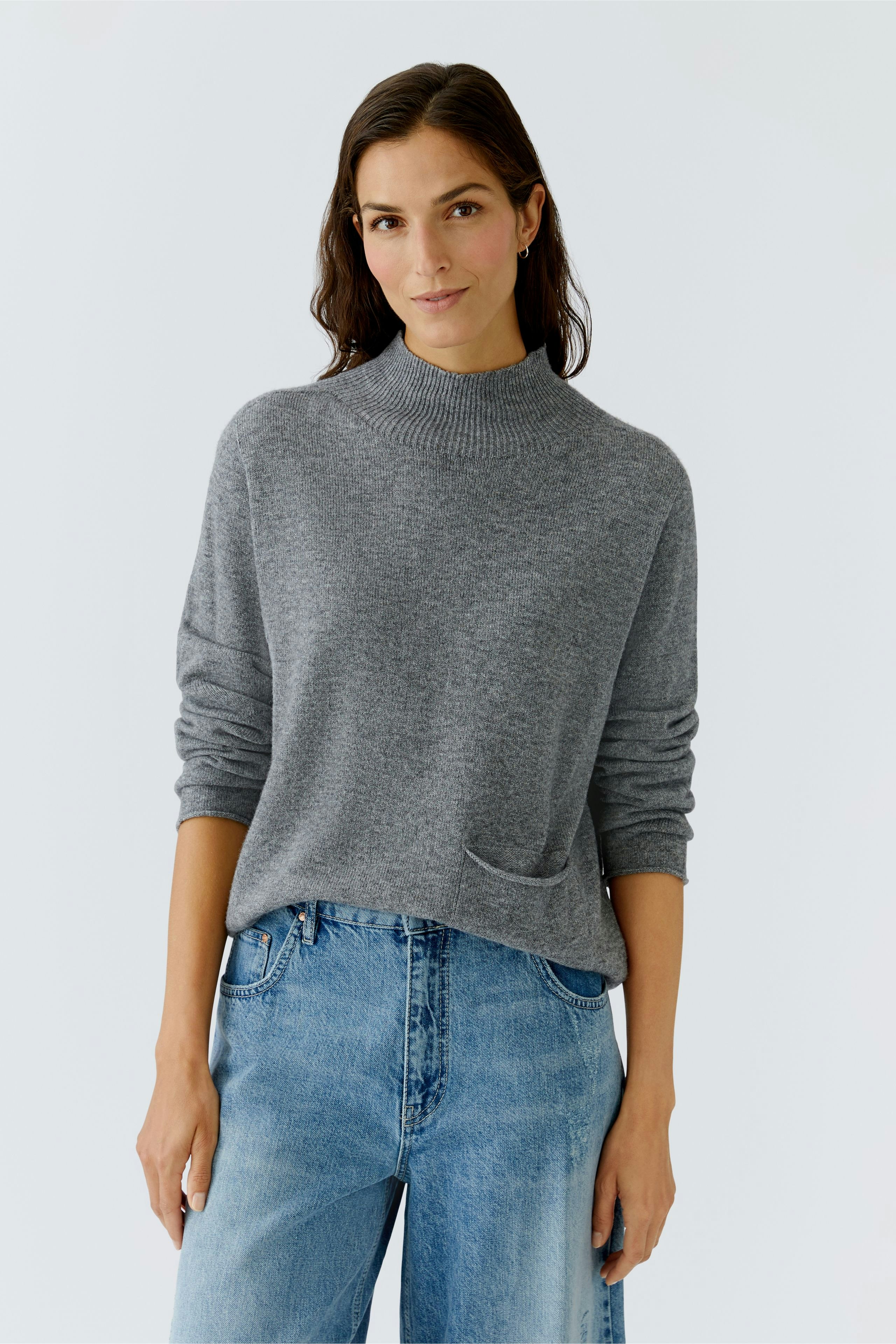 Casual women's pullover: A woman in a gray pullover with a relaxed fit and a front pocket.