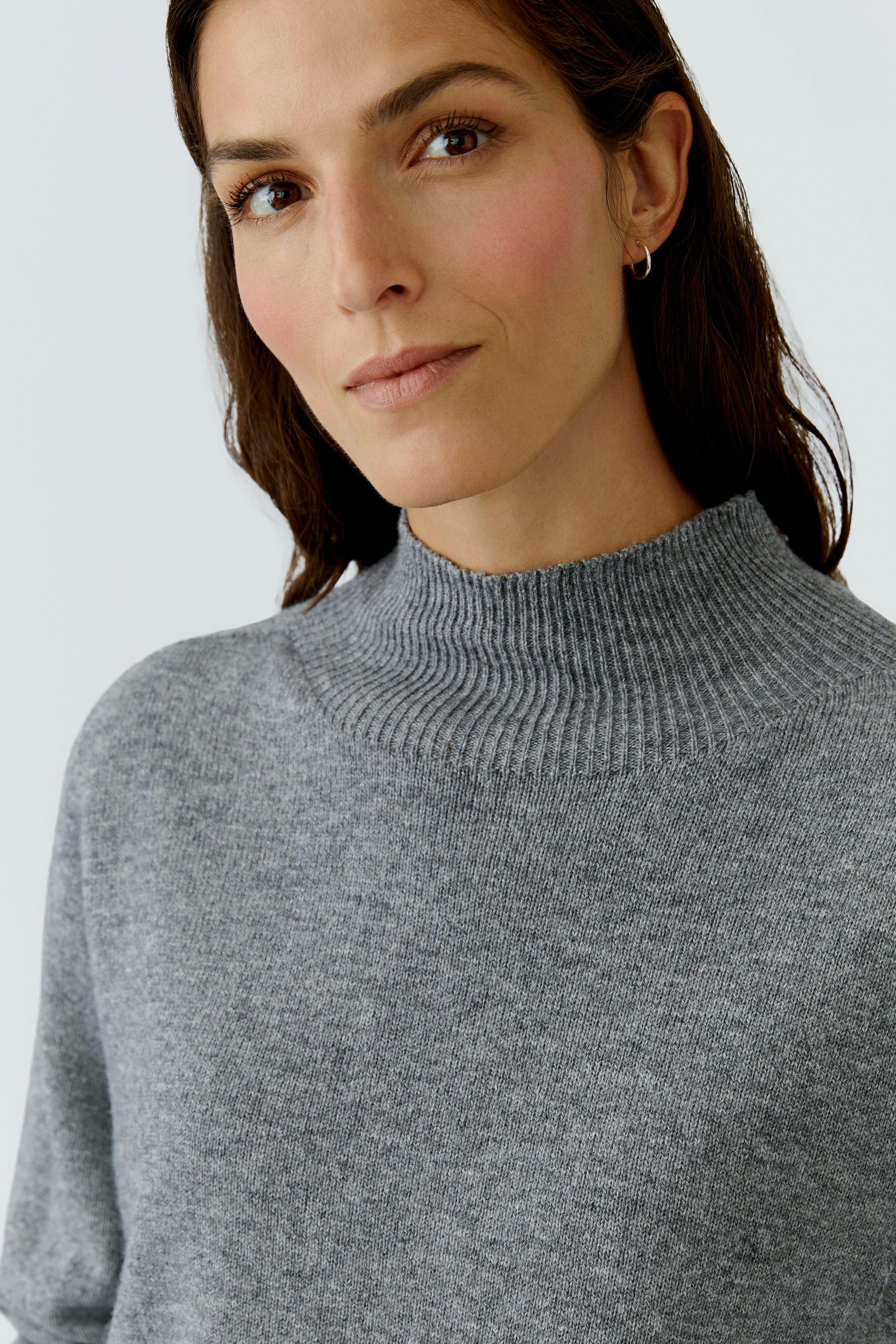 Casual women's pullover: A woman in a cozy gray pullover with a high neck, looking relaxed.