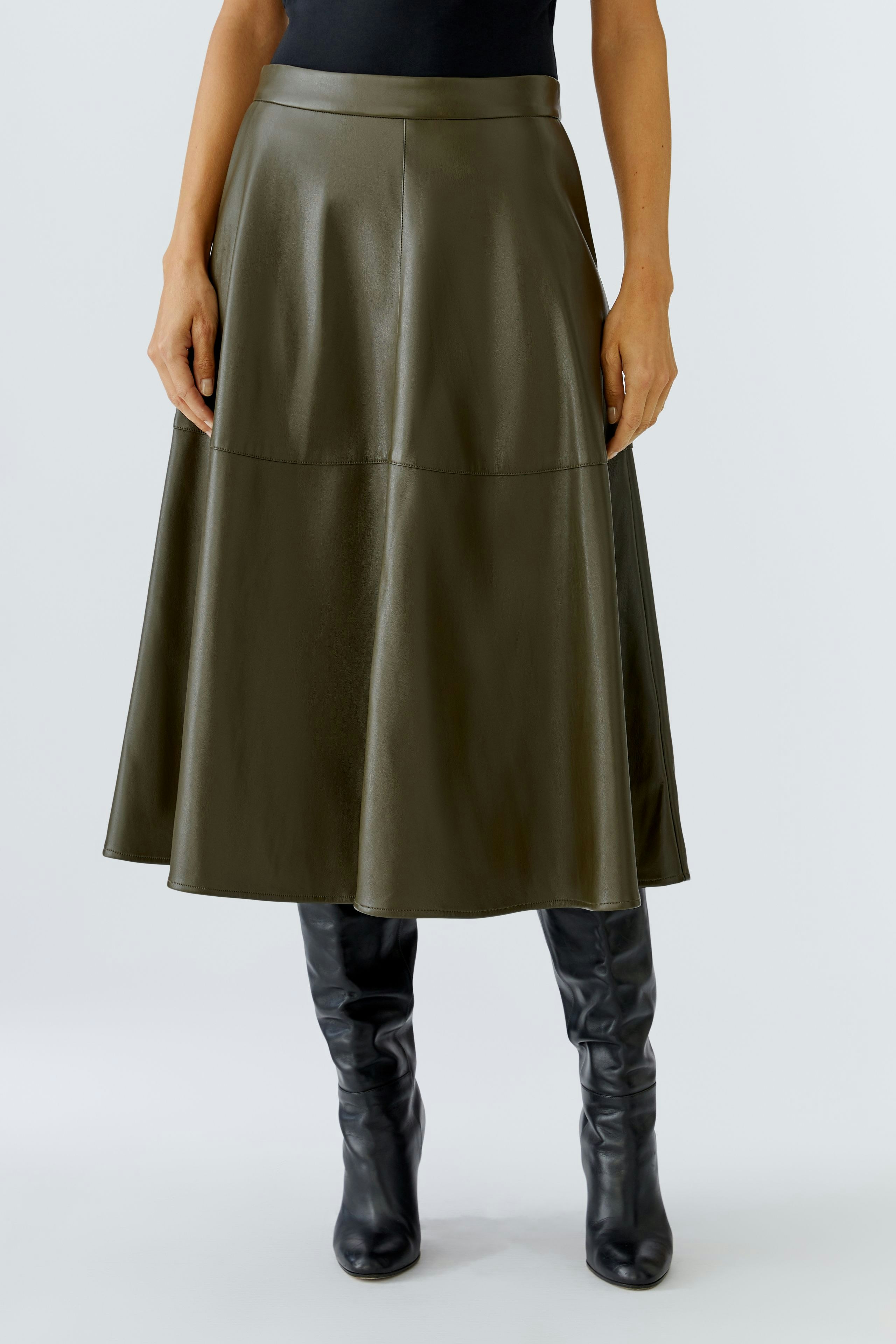 A-line skirt: Woman in a green faux leather skirt paired with knee-high black boots.
