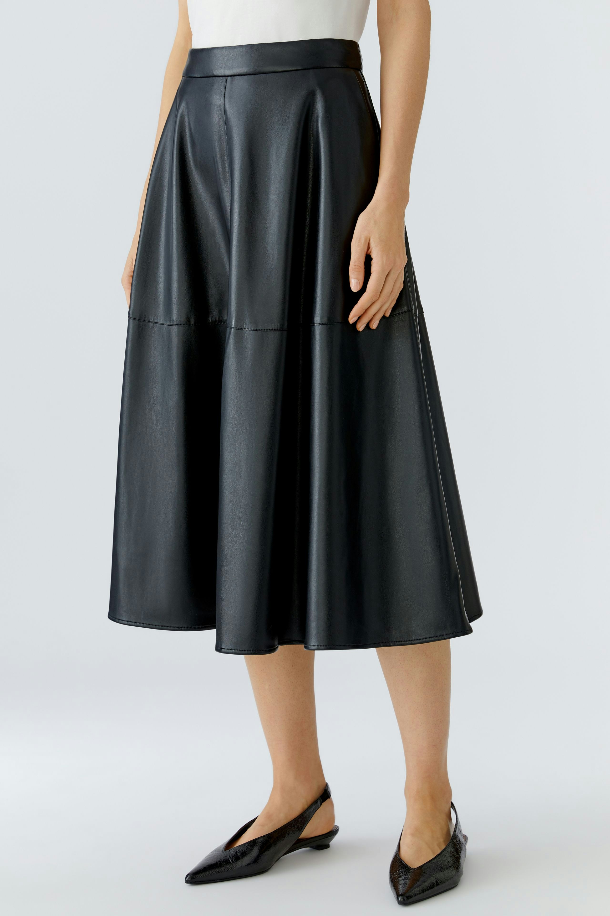 A-line skirt: Woman in a black faux leather skirt with a flared design, showcasing a modern style.