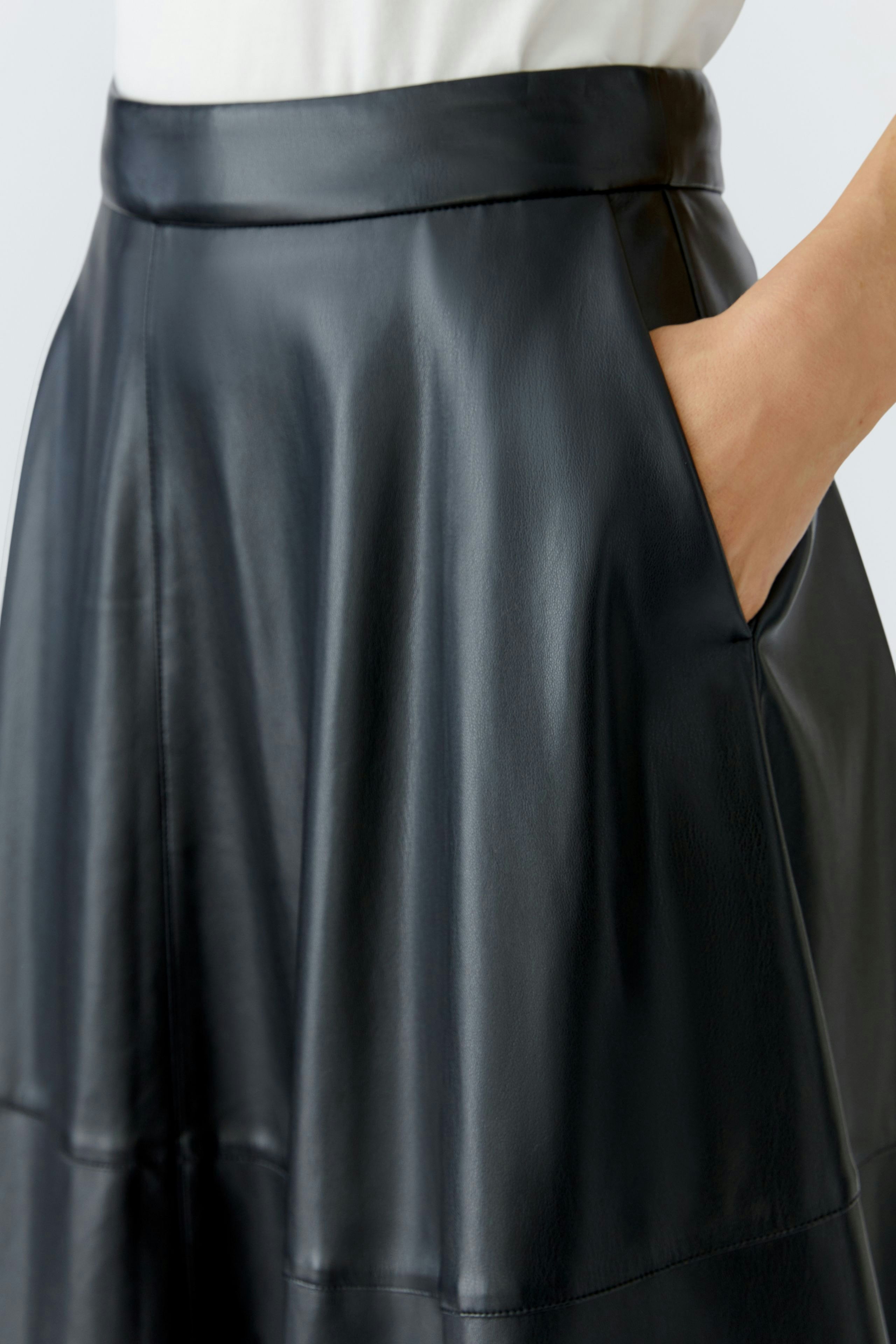 A-line skirt: Woman in a black faux leather skirt with pockets, showcasing a modern and casual style.