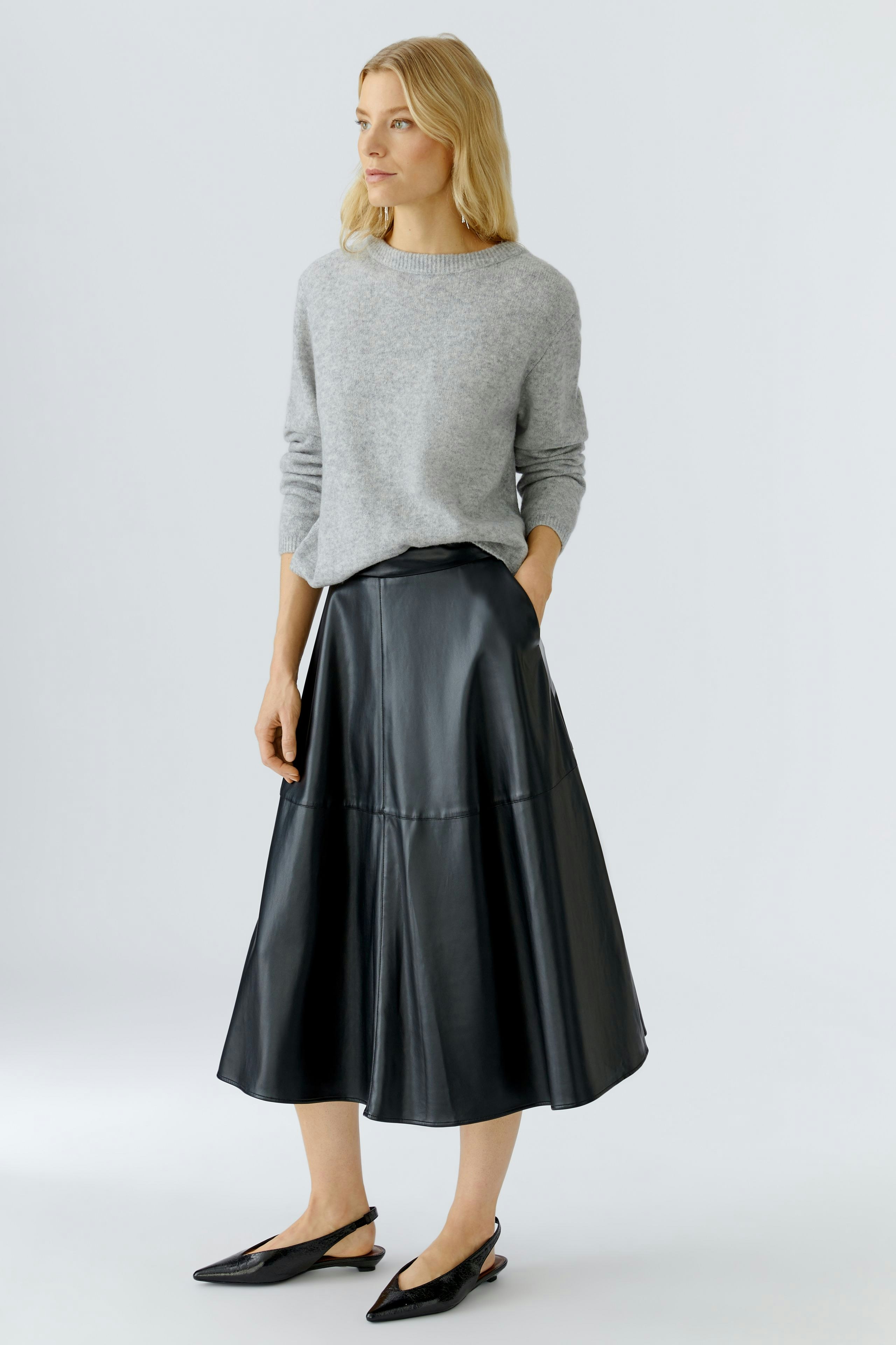 A-line skirt: Woman in a gray pullover and black A-line skirt stands confidently.