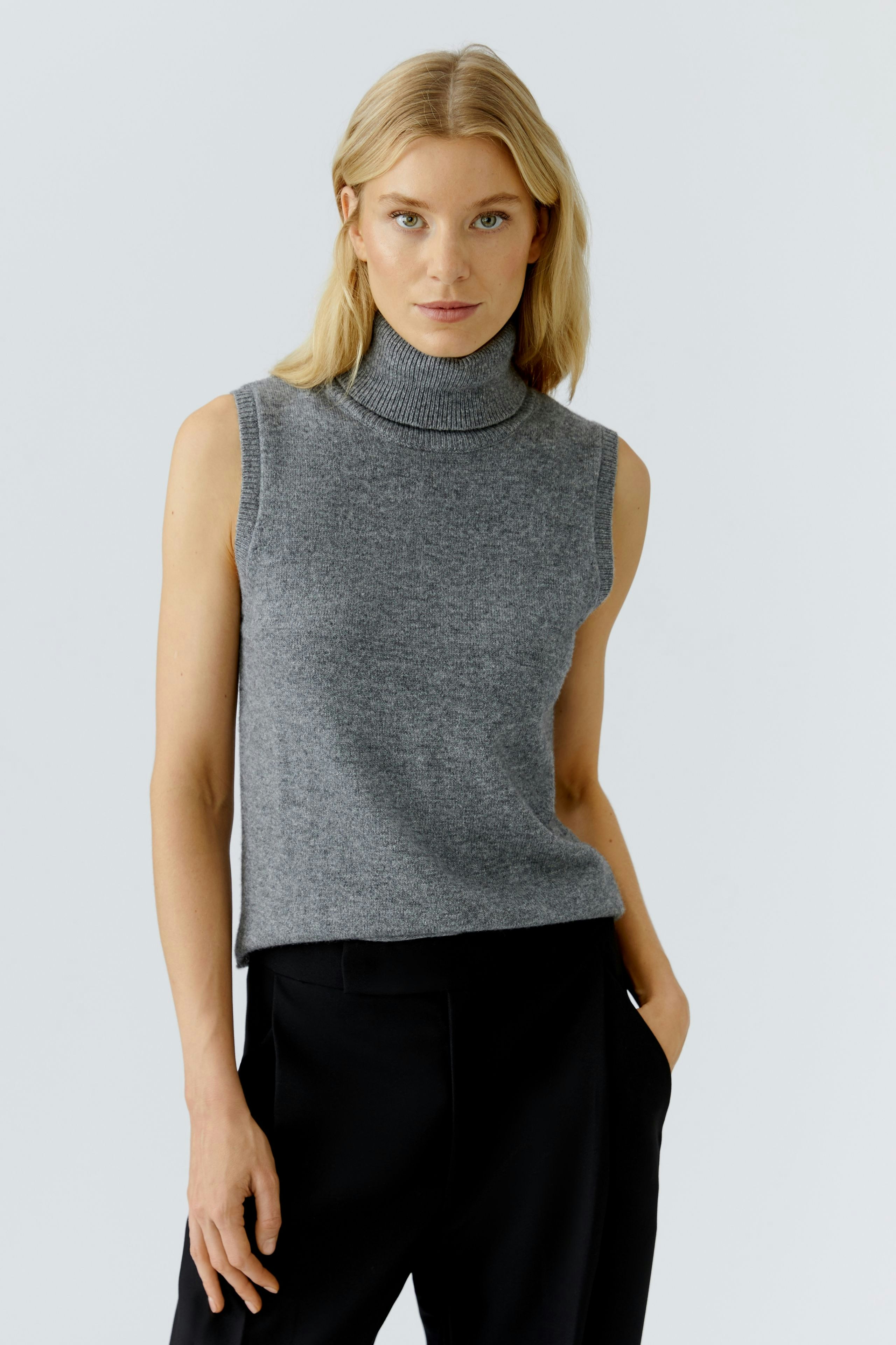 Casual women's top: A woman in a gray sleeveless pullover with a high neck, paired with black trousers.
