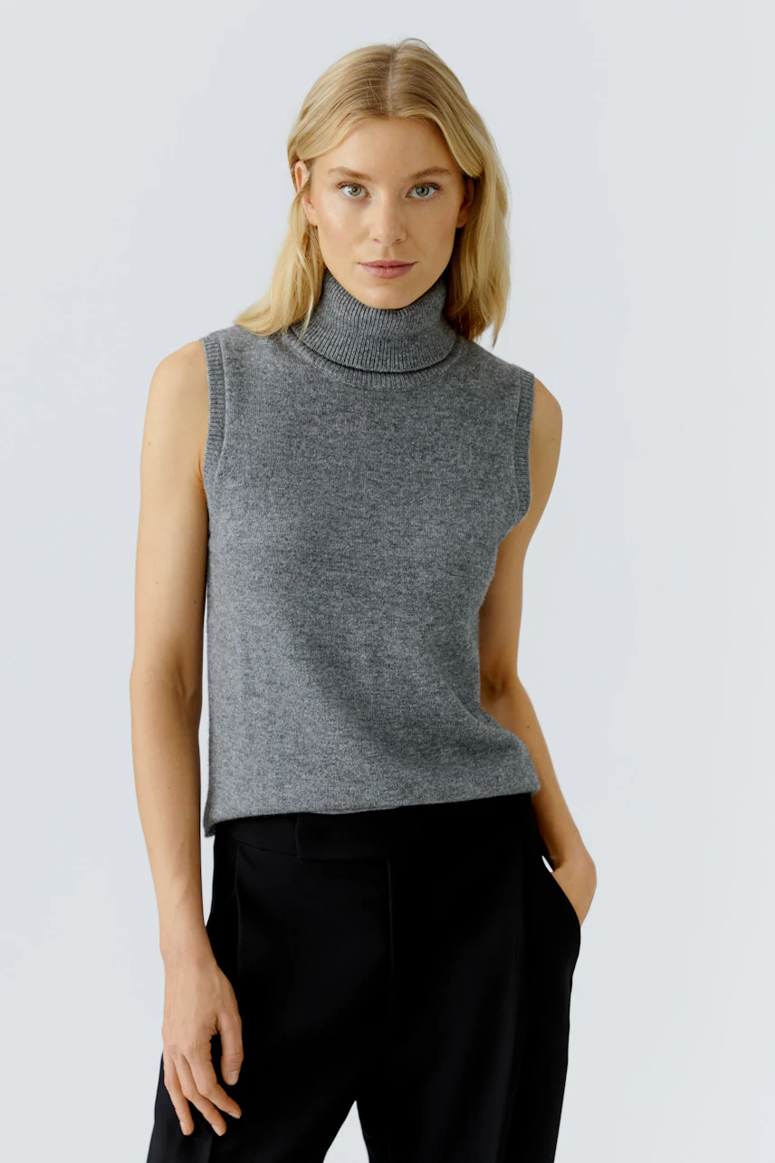 Casual women's top: A woman in a gray sleeveless pullover with a high neck, paired with black trousers.