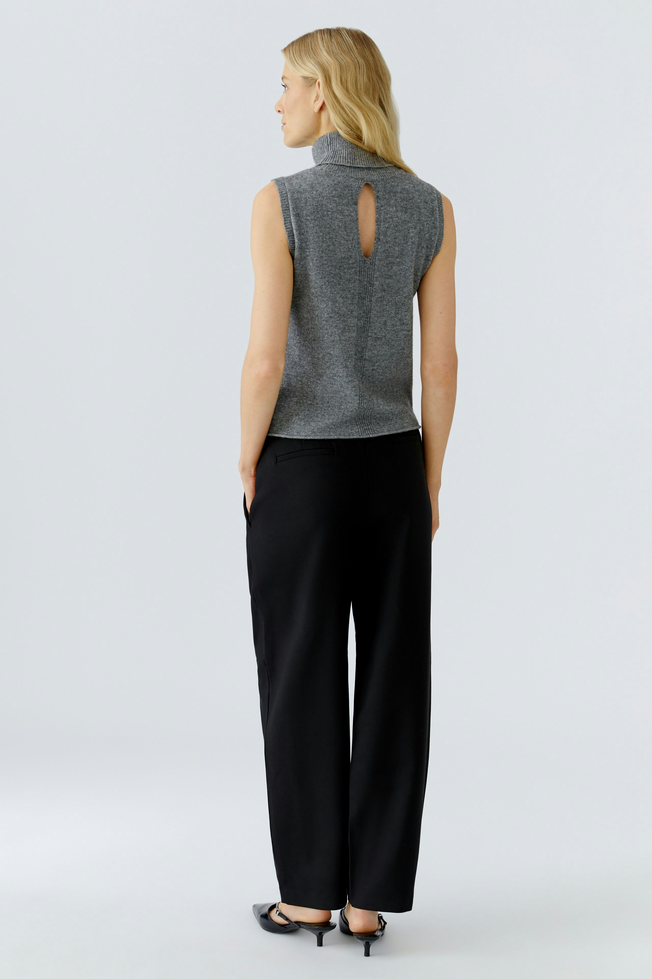 Casual women's top: Young woman in a gray sleeveless top with a keyhole detail, paired with black trousers.