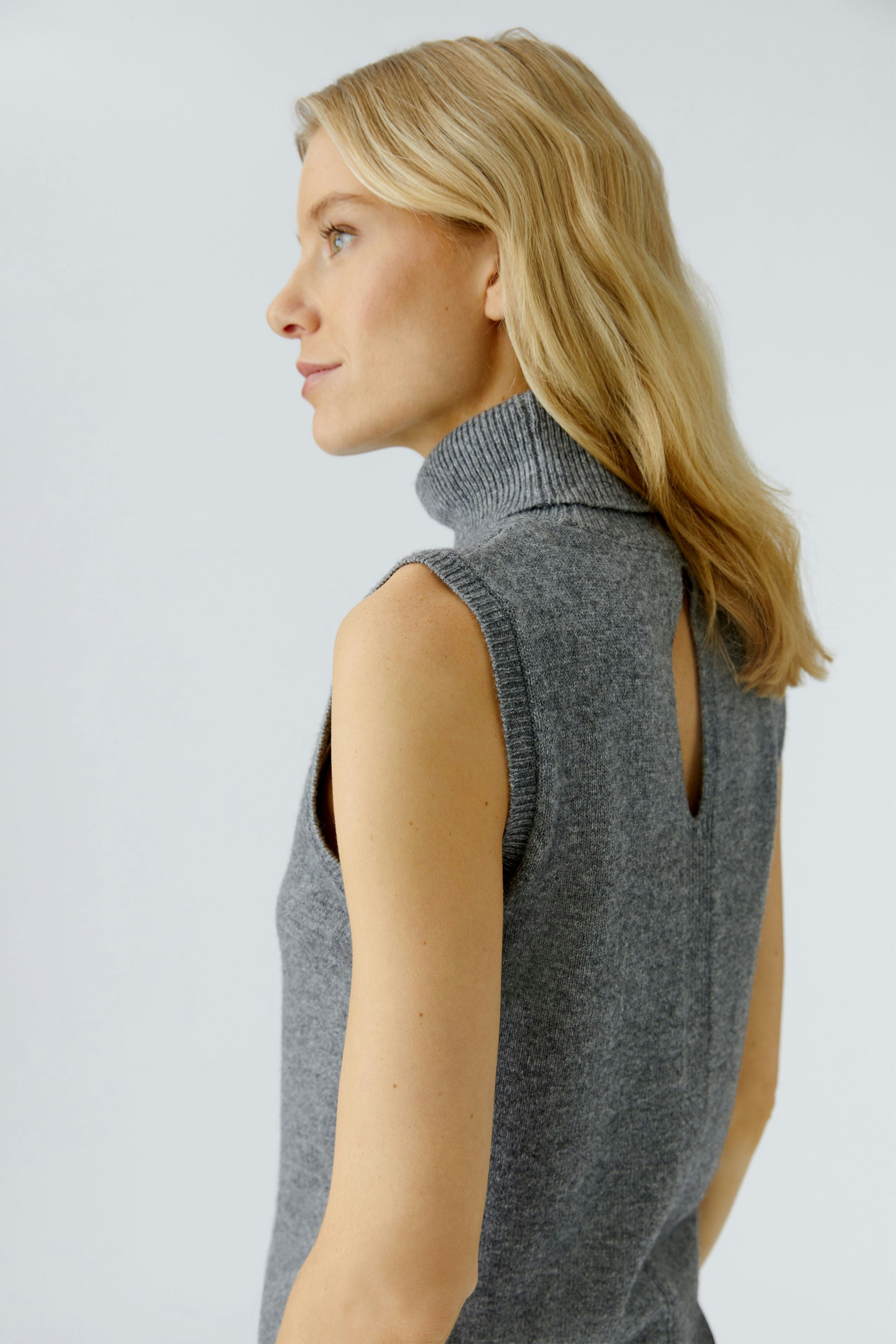 Stylish women's top: A woman in a gray sleeveless top with a high collar, showcasing a modern look.