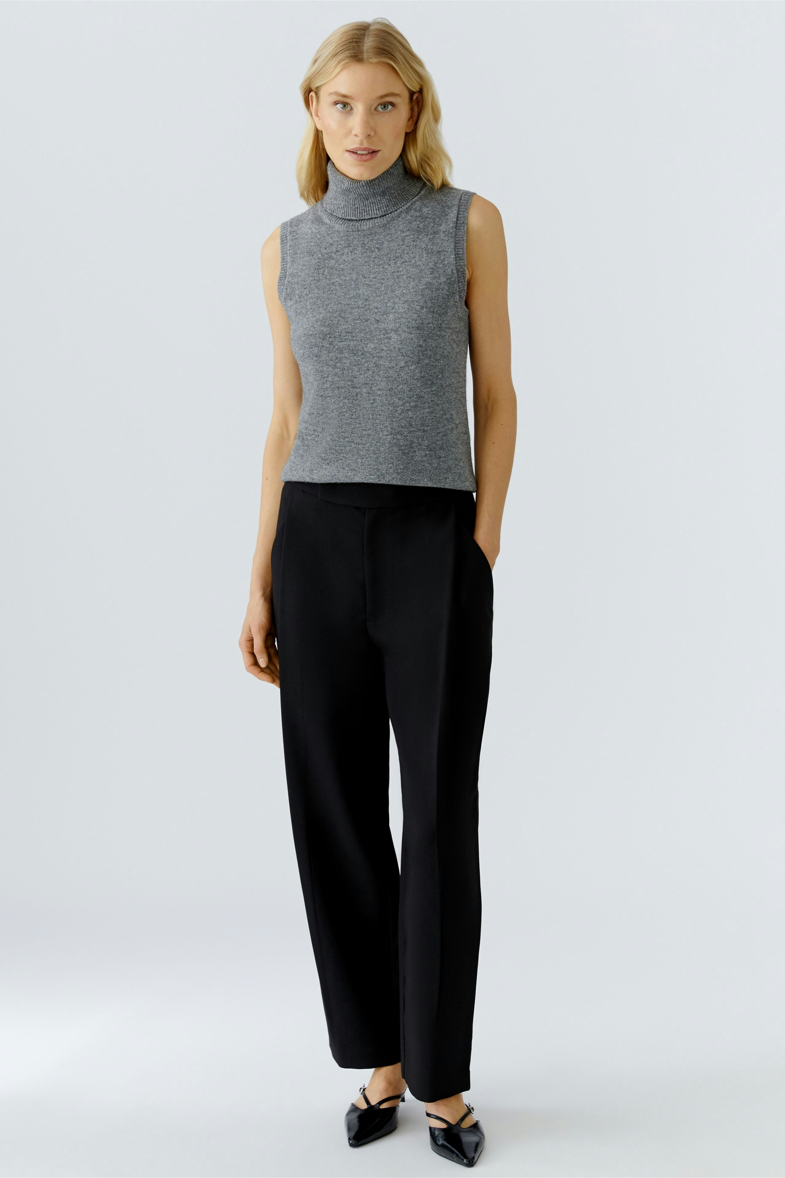 Casual women's top: Young woman in a gray sleeveless pullover paired with black trousers.