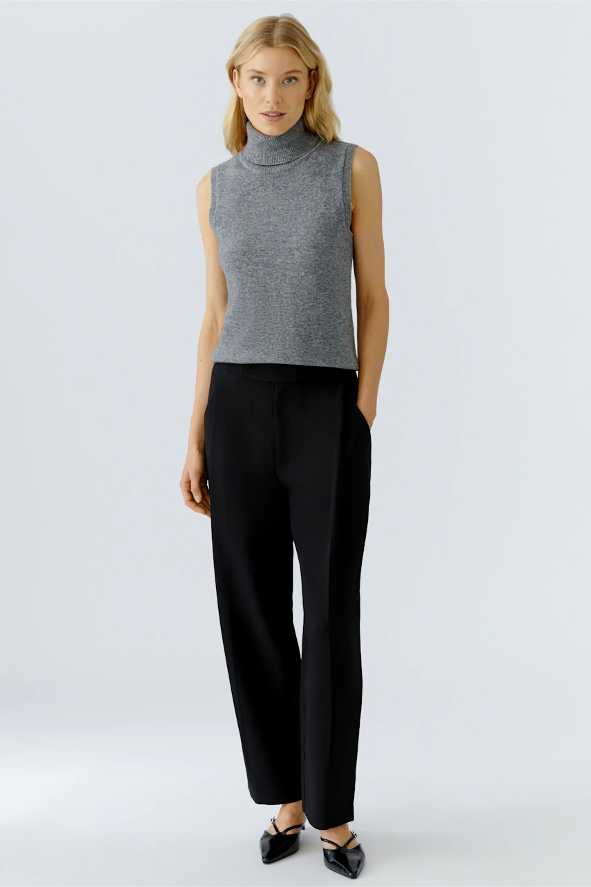 Casual women's top: Young woman in a gray sleeveless pullover paired with black trousers.