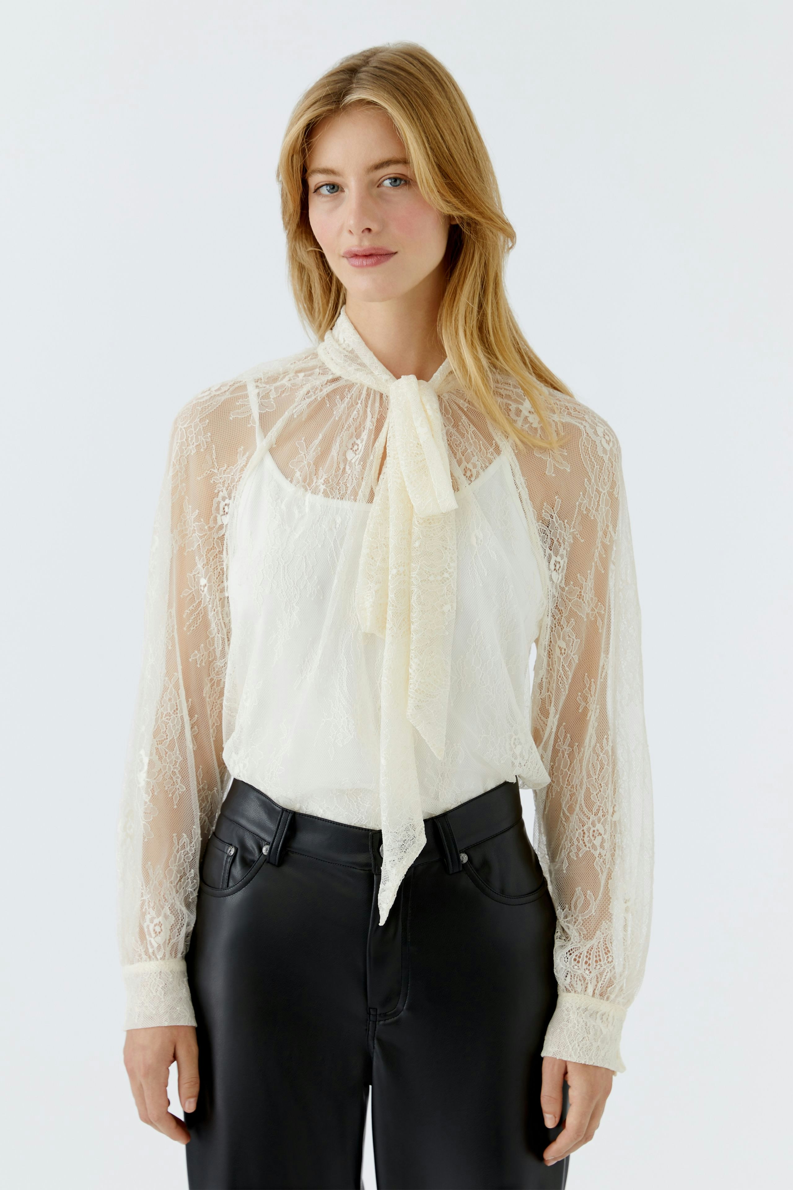 Lightweight women's blouse with sheer sleeves and a tie detail, paired with casual jeans.
