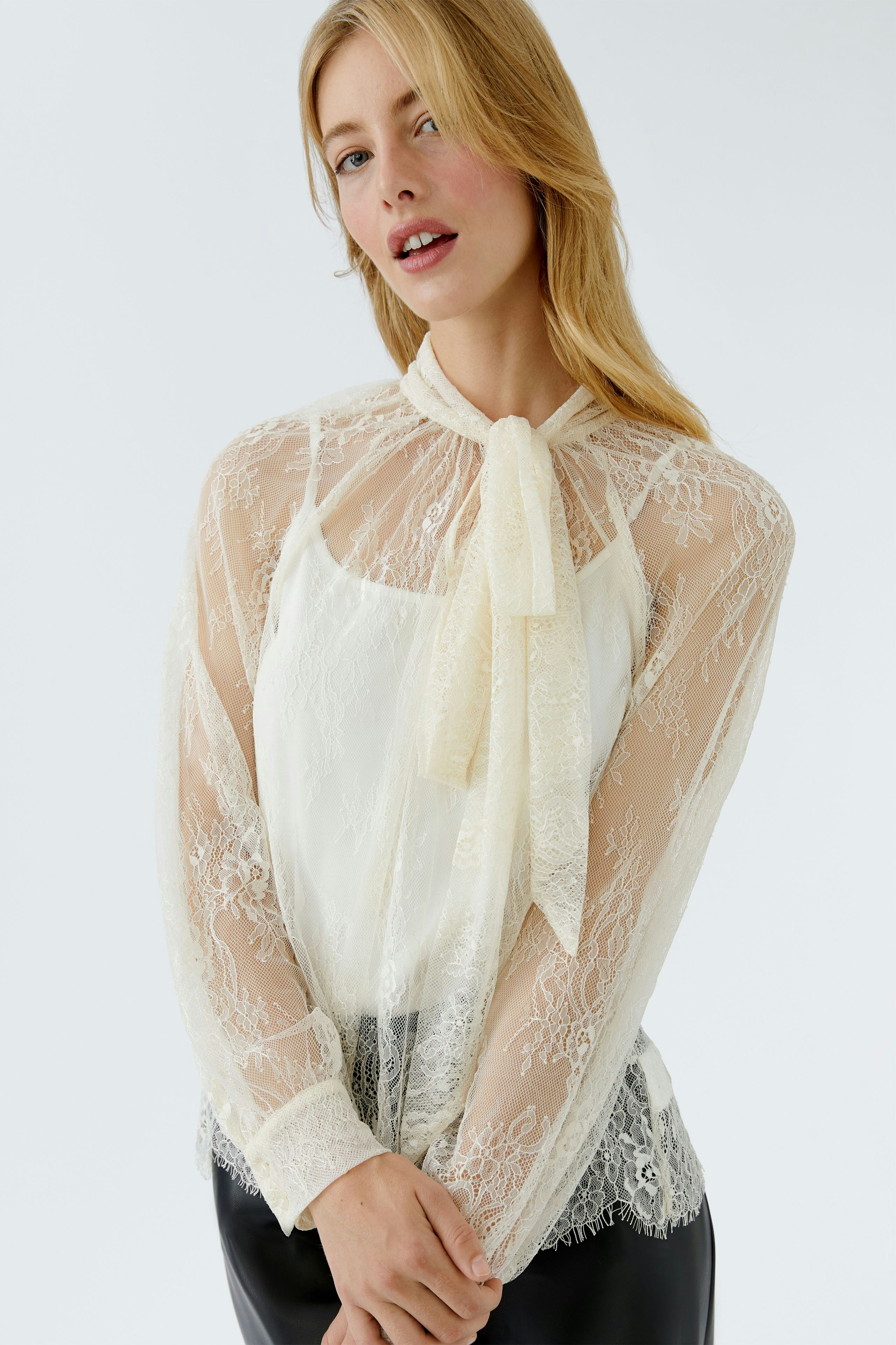 Lightweight blouse: Woman in a sheer white blouse with a bow tie and lace details, paired with denim.