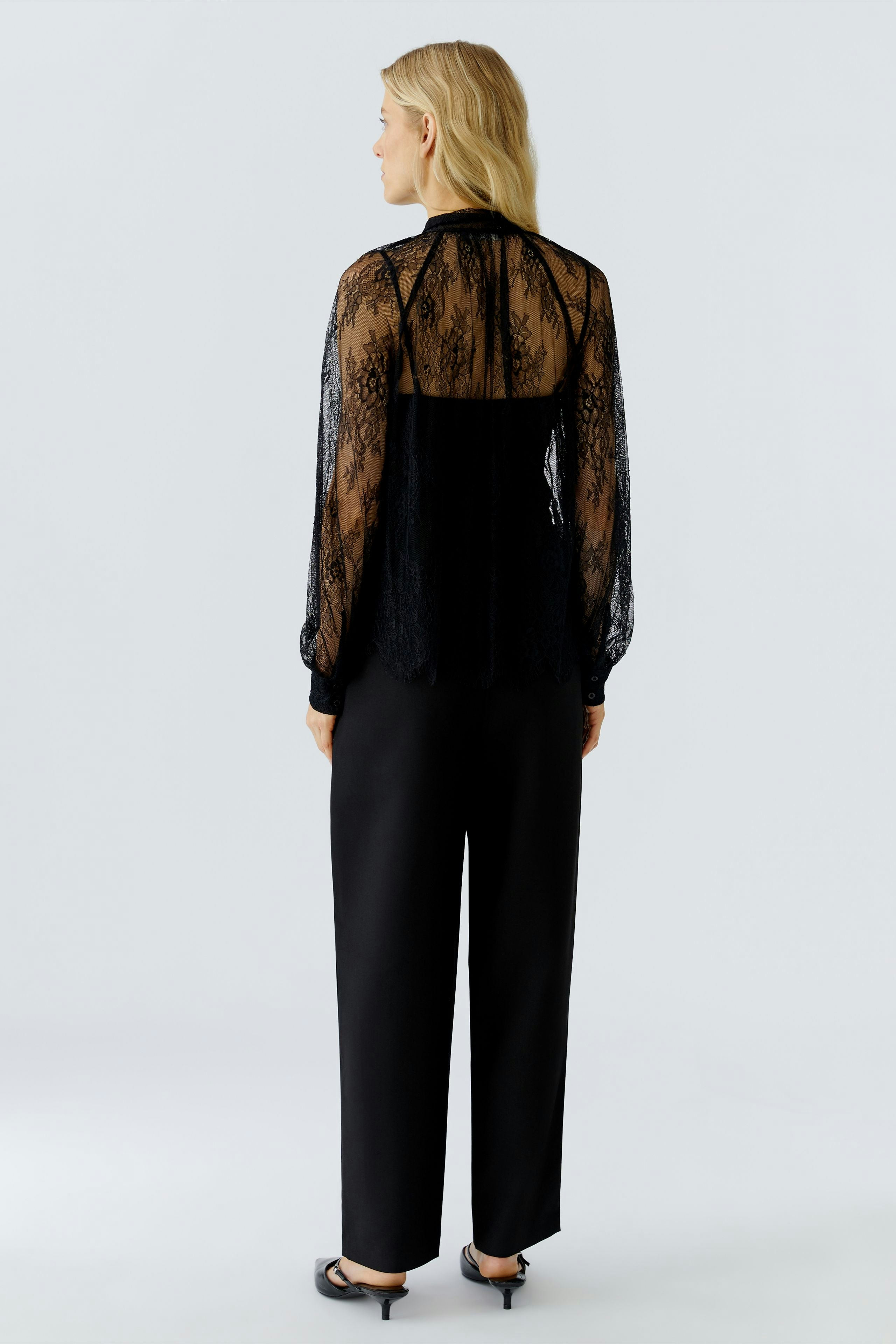 Sheer black blouse: Woman in a delicate lace blouse with billowy sleeves, paired with sleek trousers.