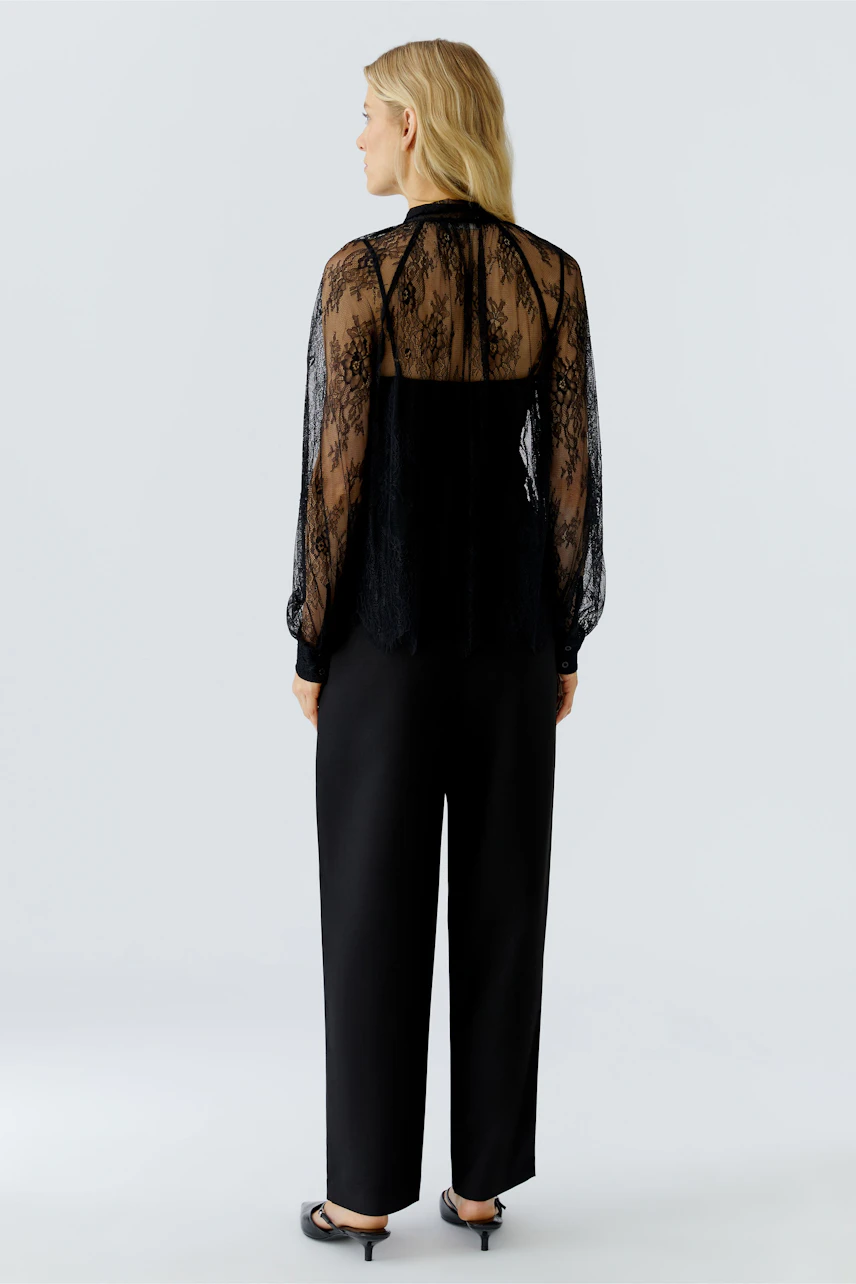Sheer black blouse: Woman in a delicate lace blouse with billowy sleeves, paired with sleek trousers.