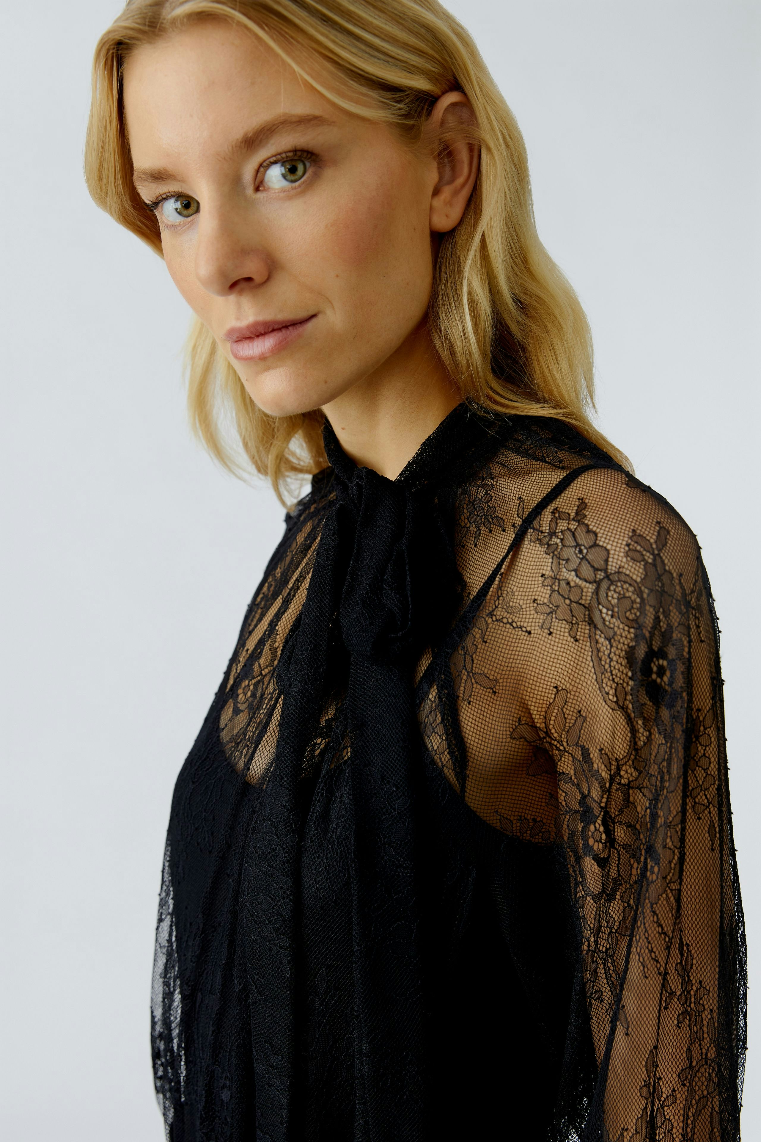 Black lace blouse: Woman in a sheer blouse with a bow tie detail, showcasing a stylish look.