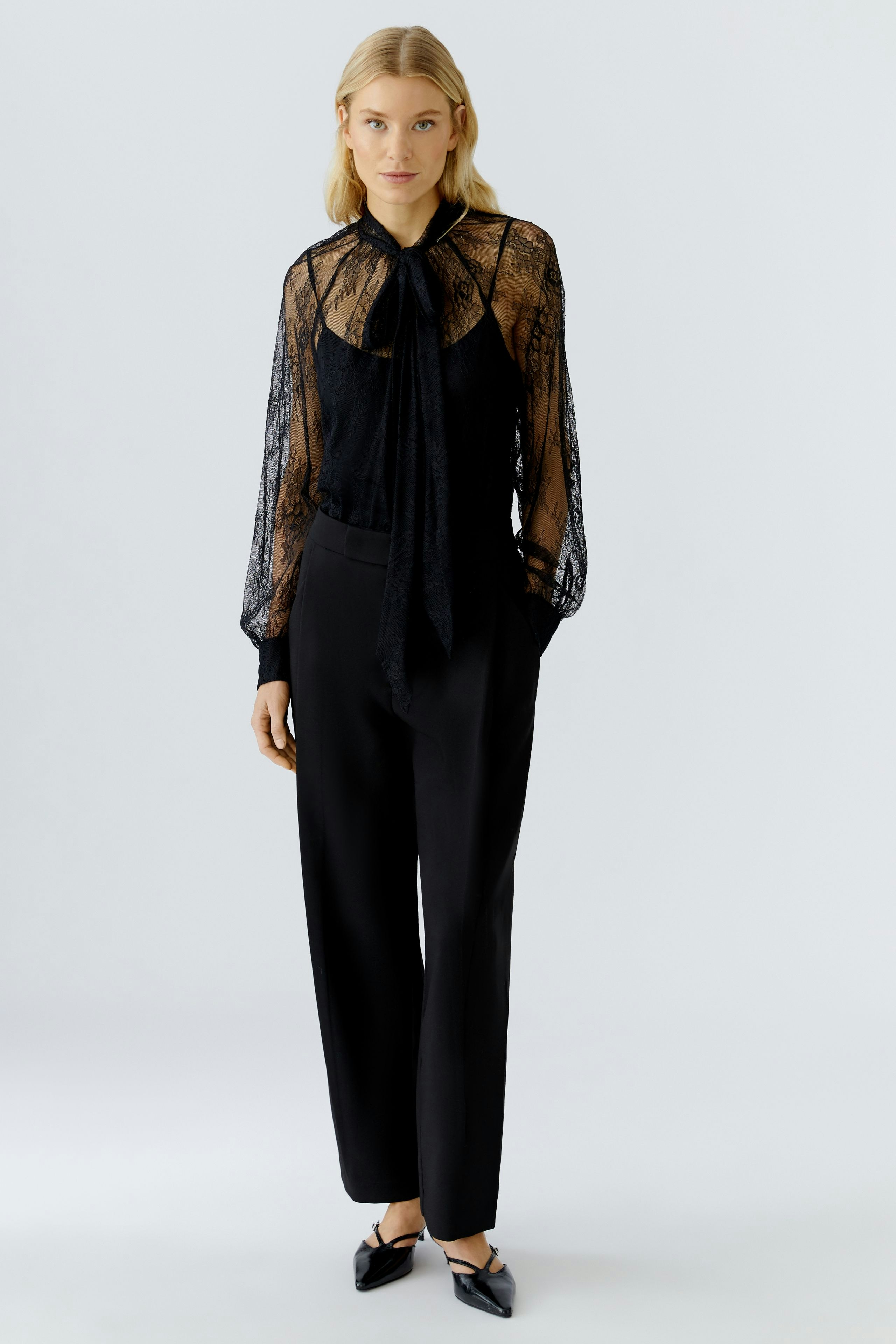 Chic black blouse: Woman in a sheer lace blouse with a tie detail, paired with tailored trousers.