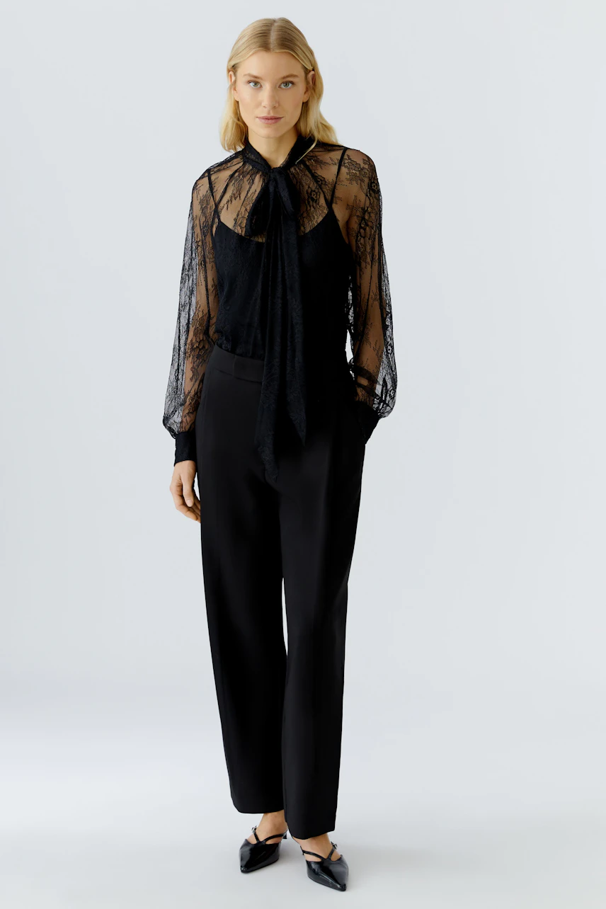 Chic black blouse: Woman in a sheer lace blouse with a tie detail, paired with tailored trousers.