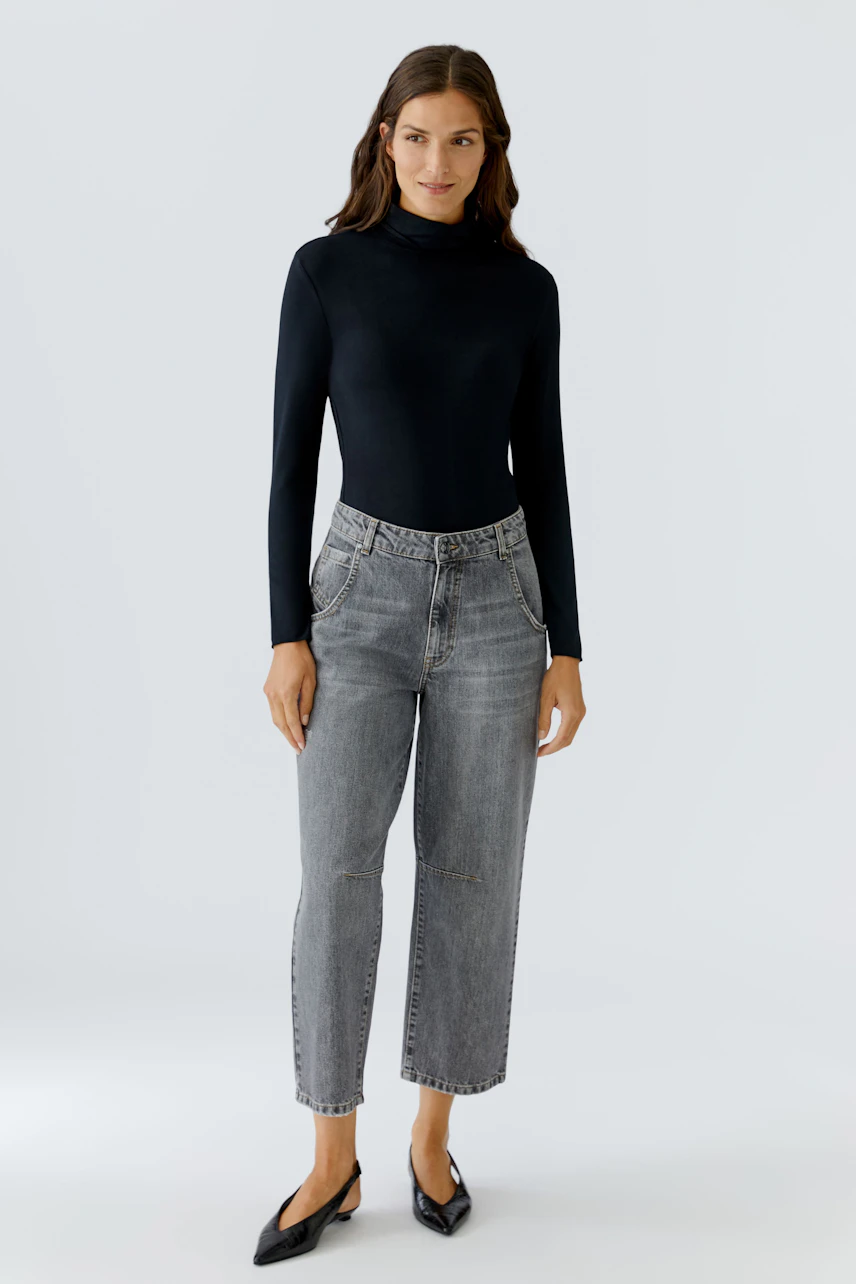 Casual women's long-sleeve shirt: A woman in a fitted black top paired with gray jeans, exuding a relaxed vibe.