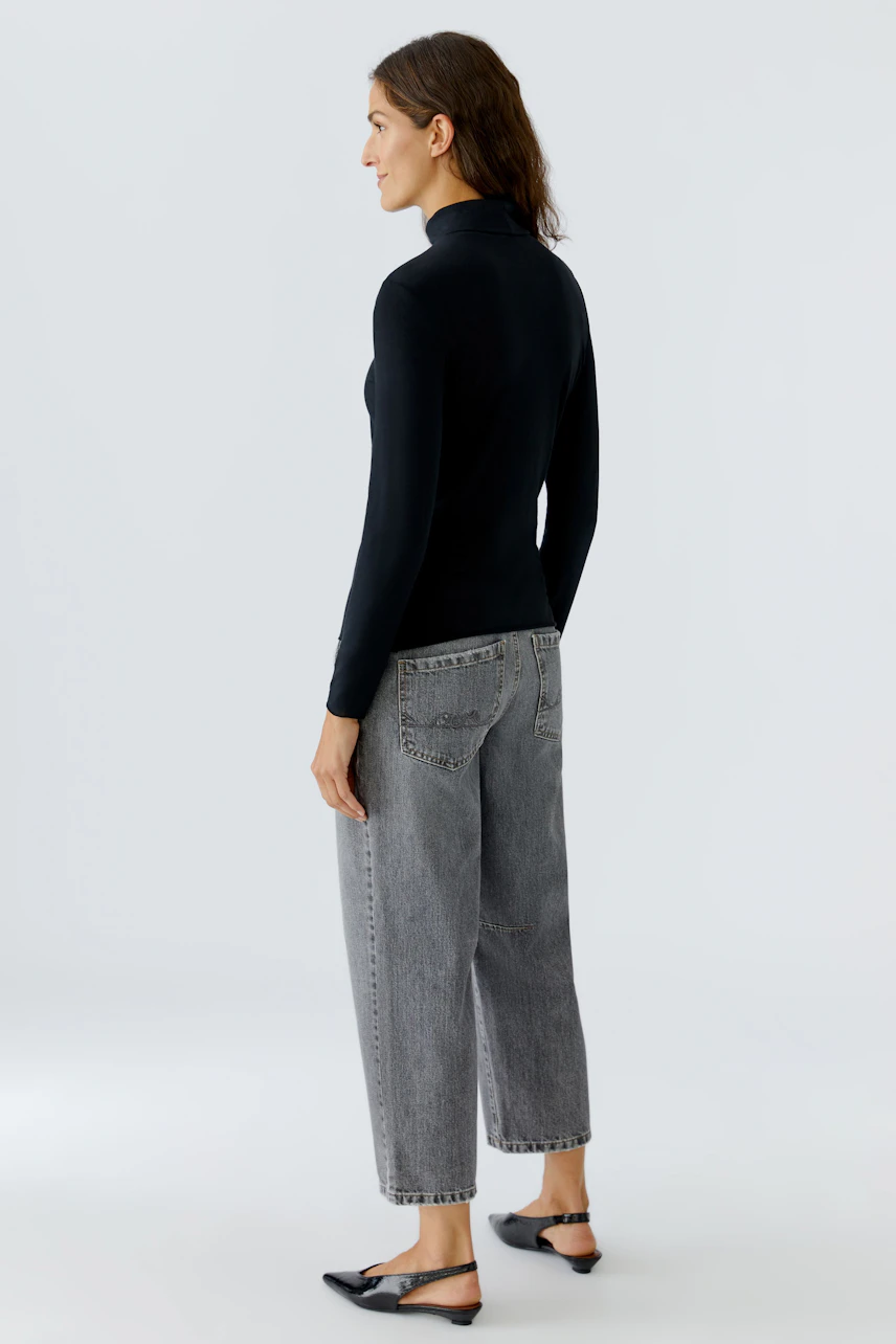 Long-sleeve shirt: Woman wearing a fitted black pullover with a high collar, paired with relaxed jeans.