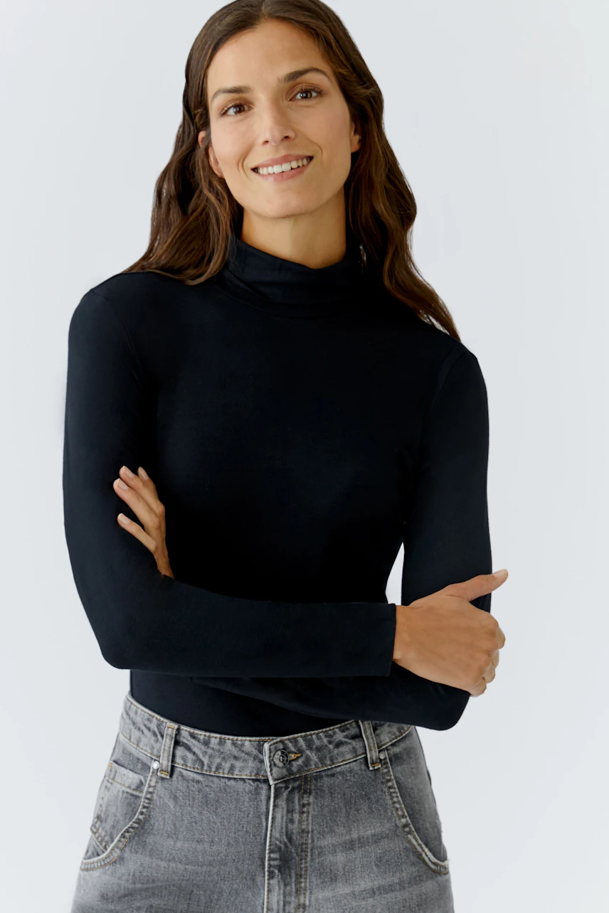 Casual women's long-sleeve shirt: A woman in a black turtleneck top smiles confidently.