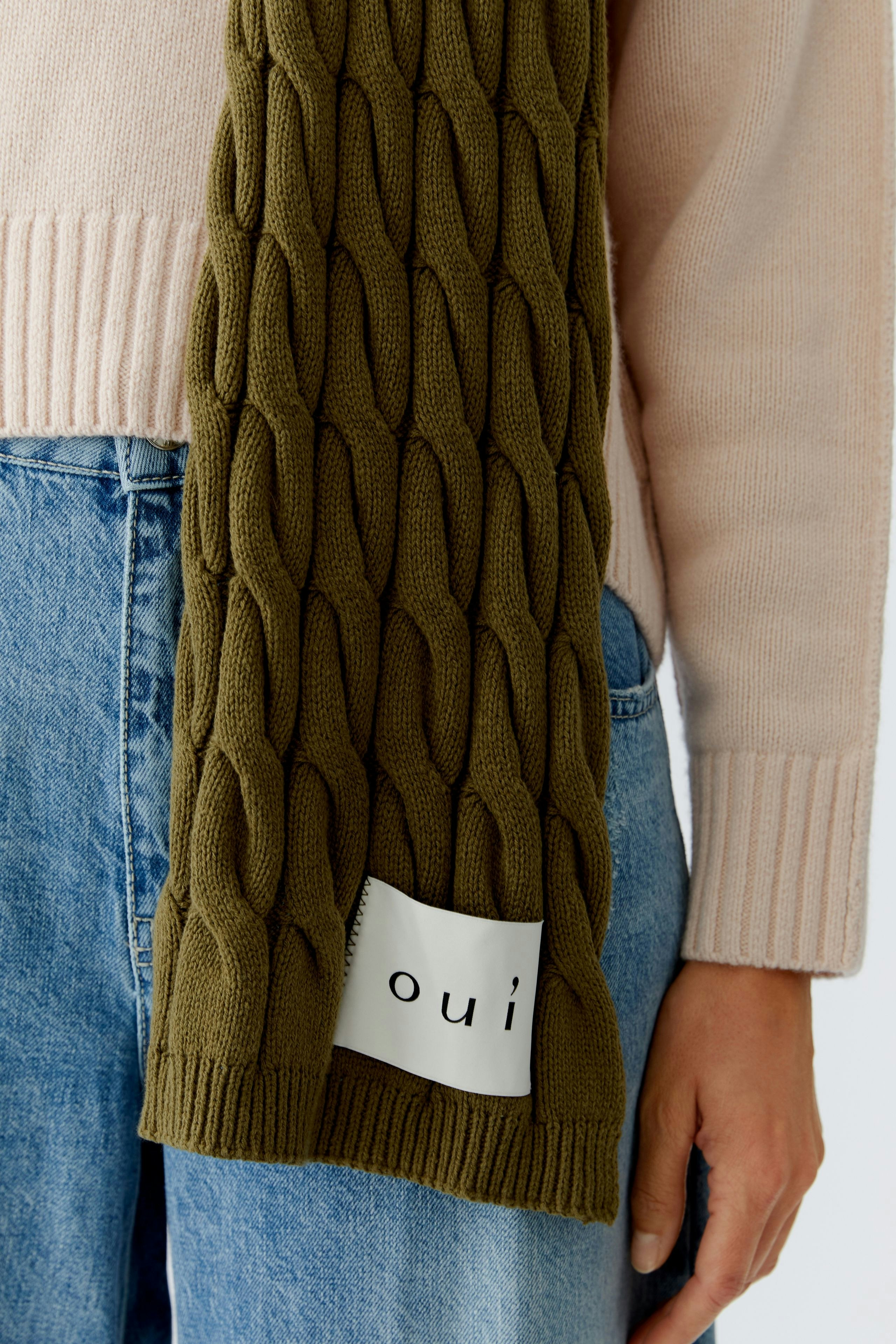 Knitted scarf: Woman wearing a textured olive green scarf, paired with a light pink pullover.