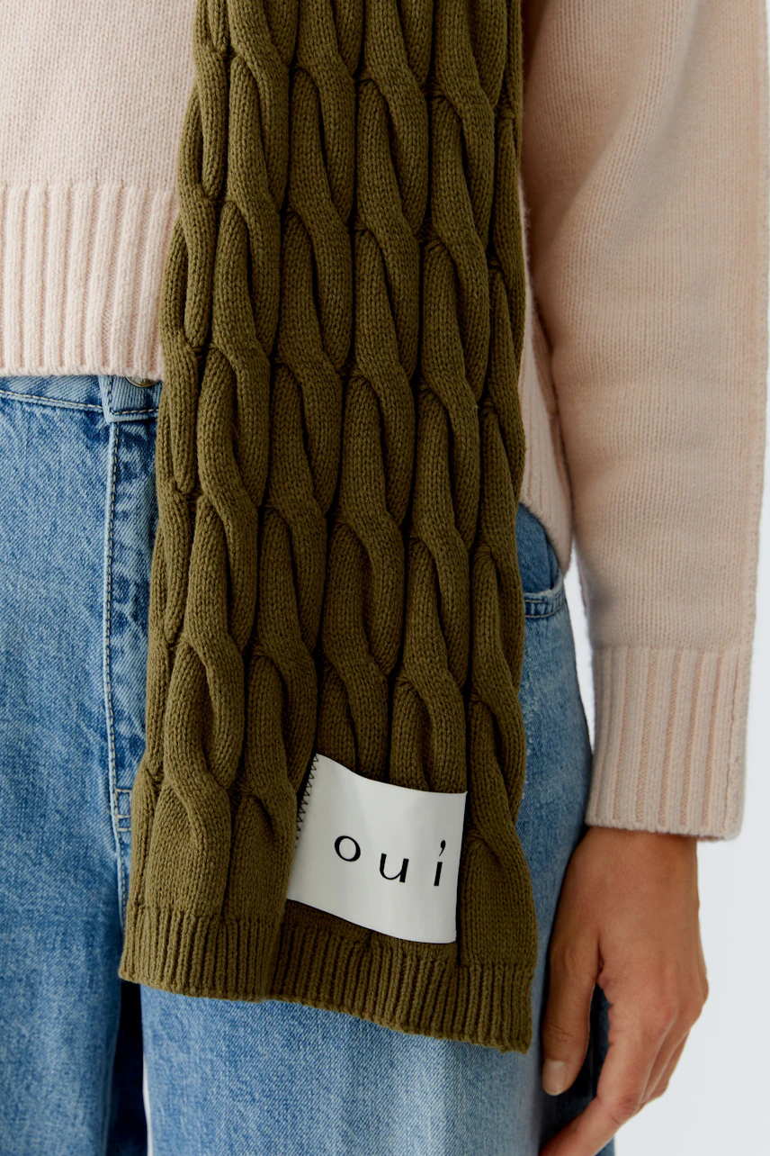 Knitted scarf: Woman wearing a textured olive green scarf, paired with a light pink pullover.