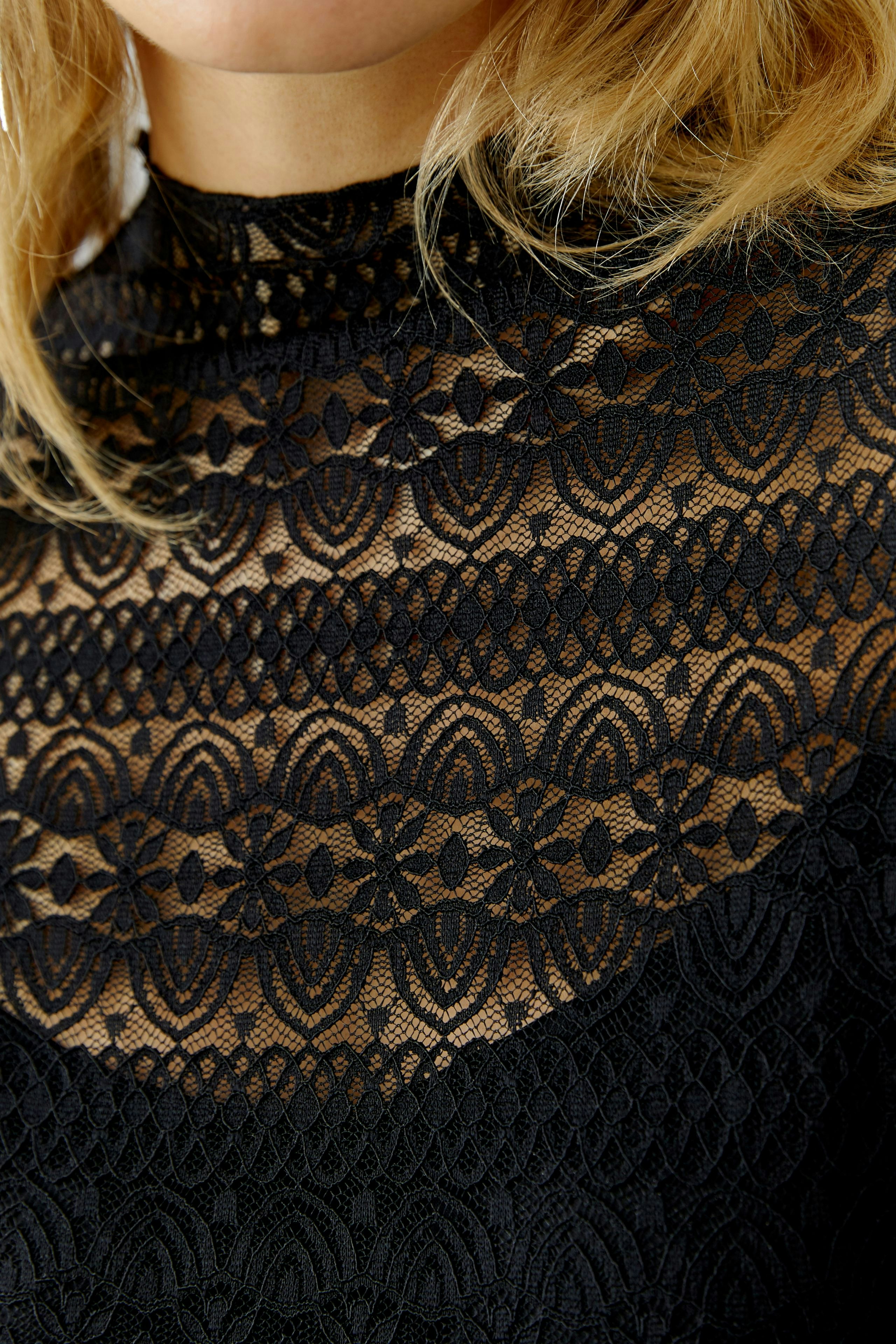 Stylish long-sleeve shirt: Woman in a black lace top with intricate patterns, showcasing a modern look.