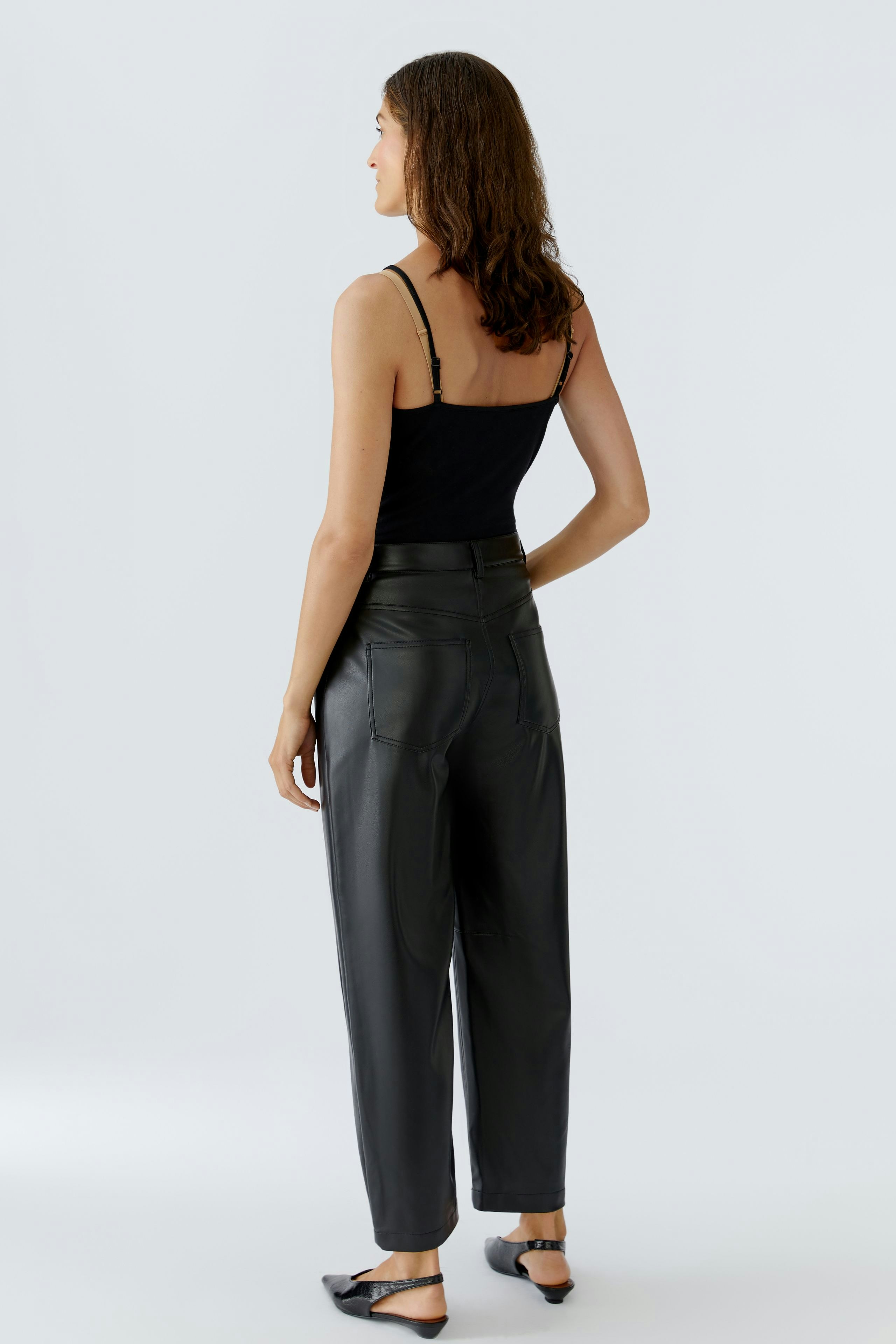 Trendy women's faux leather pants: Woman in black pants with a relaxed fit, showcasing a modern style.
