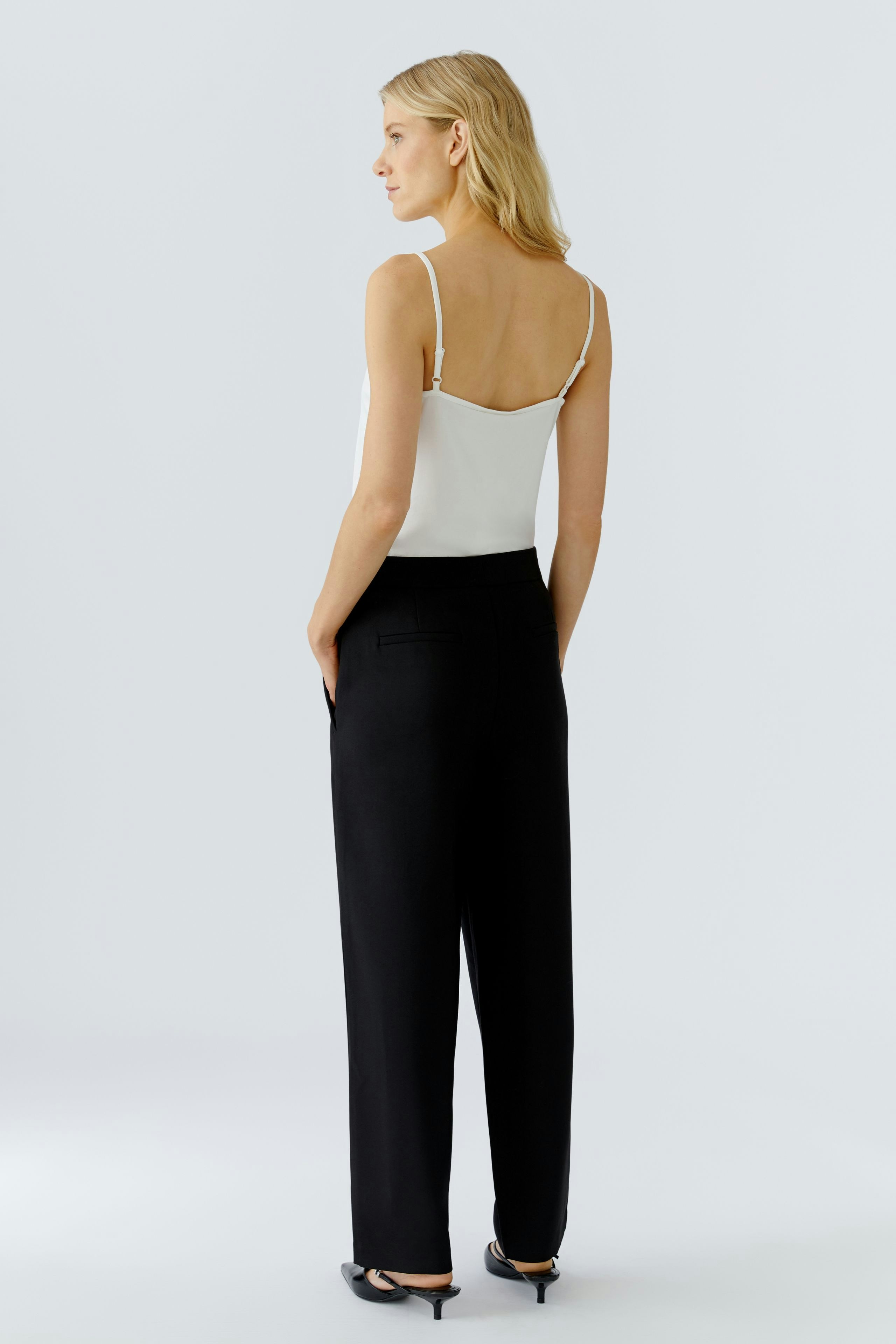 Stylish women's pleated trousers: A woman in black trousers and a white top, showcasing a modern look.